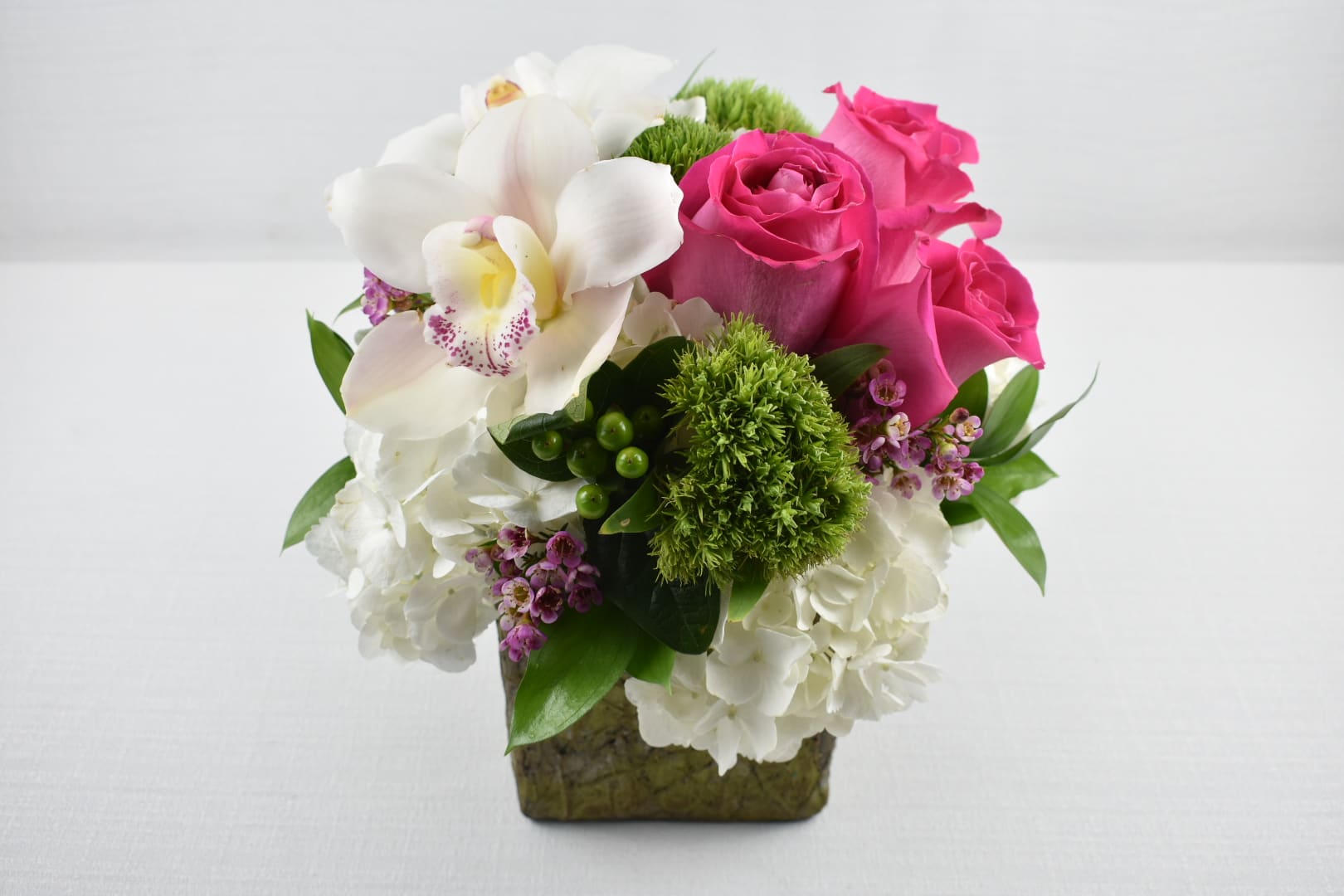 Compact arrangement of white hydrangeas, pink roses, and a white orchid in a green cube vase