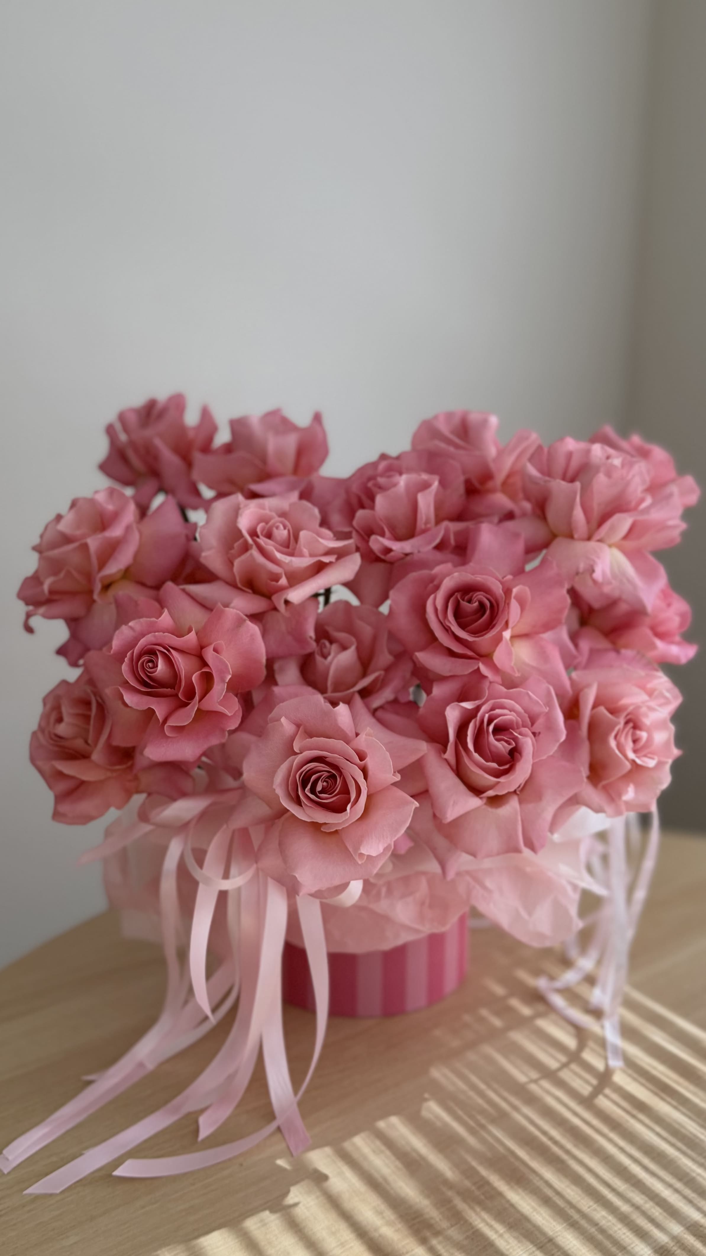 Pink rose bouquet in a striped round box with ribbon tails