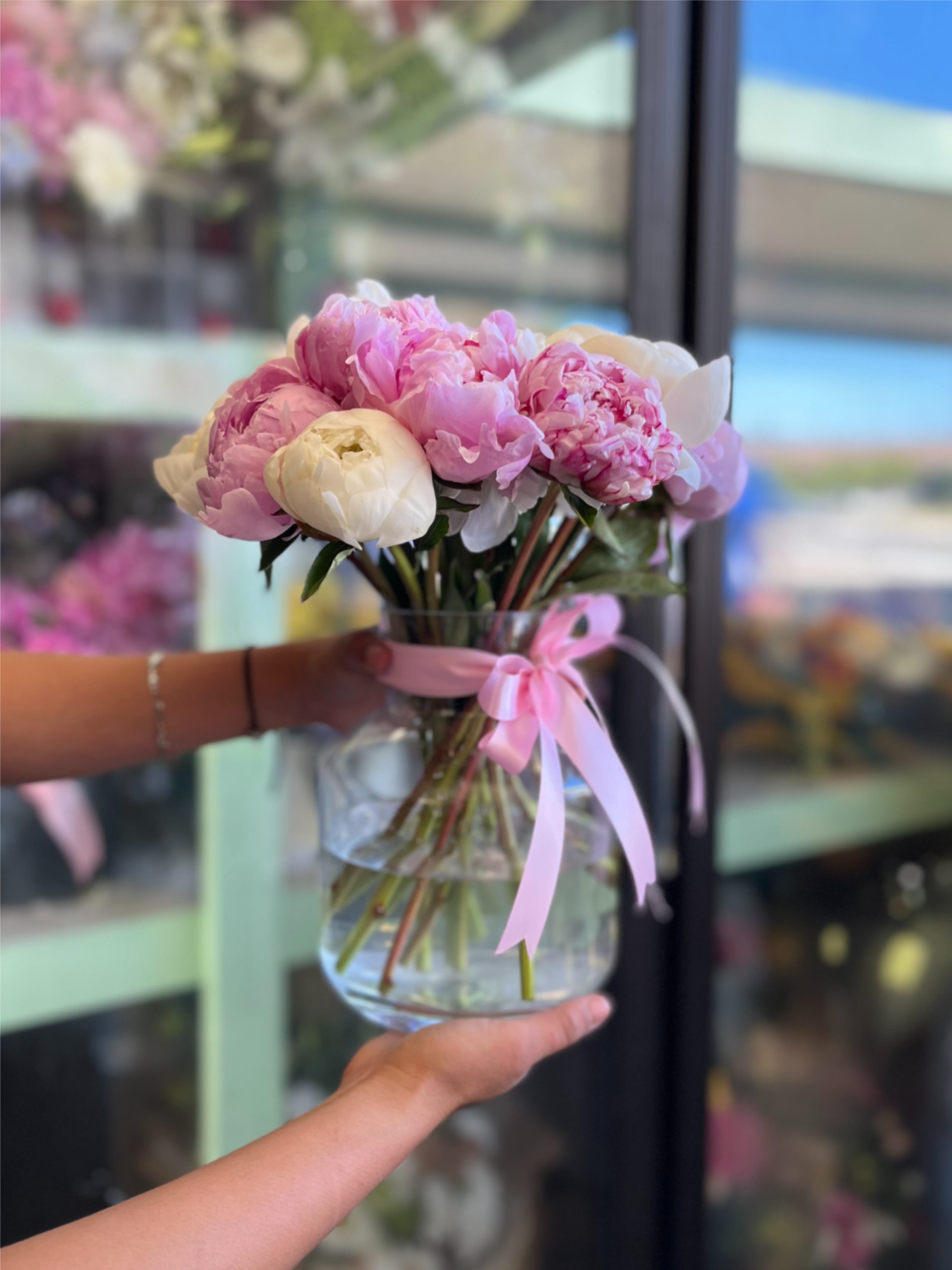Peony Vase Small Arrangement - A rounded cluster of 12 pink and white peonies arranged in a clear glass vase creates a soft, lush centerpiece perfect for birthdays, anniversaries, or Mother's Day that will make the person you're thinking of feel truly celebrated. Tied with a delicate pink ribbon, this small peony arrangement showcases each full, layered bloom with a gift-ready elegance and fresh, romantic appeal.