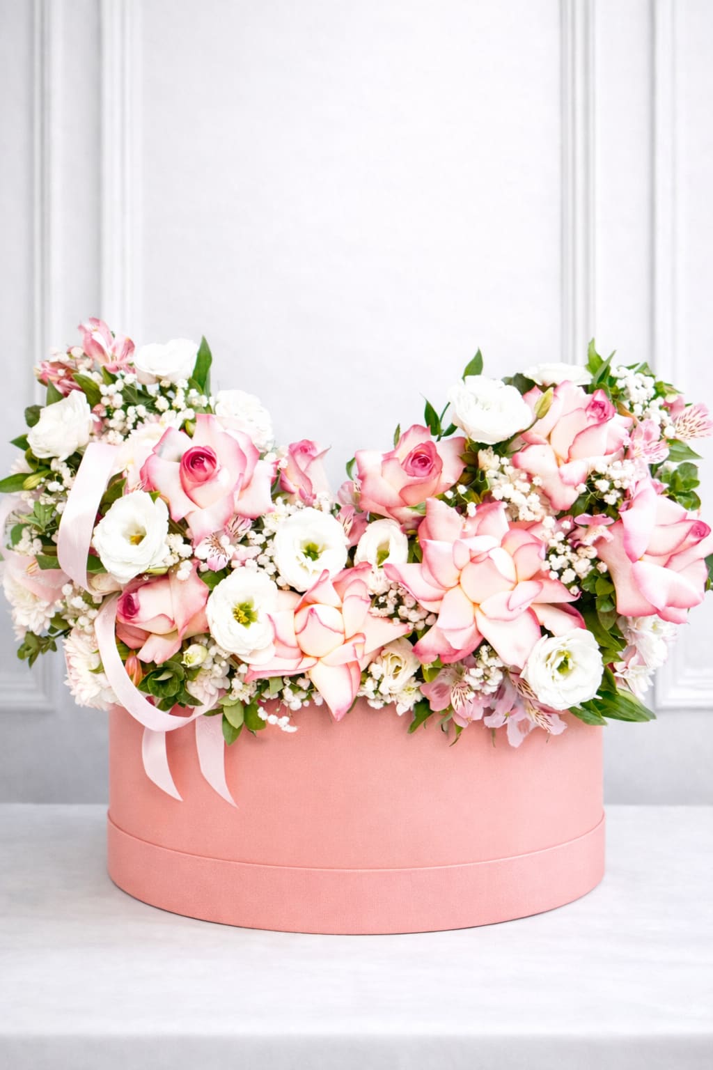 Pink and white roses arranged in a round pink box with ribbon