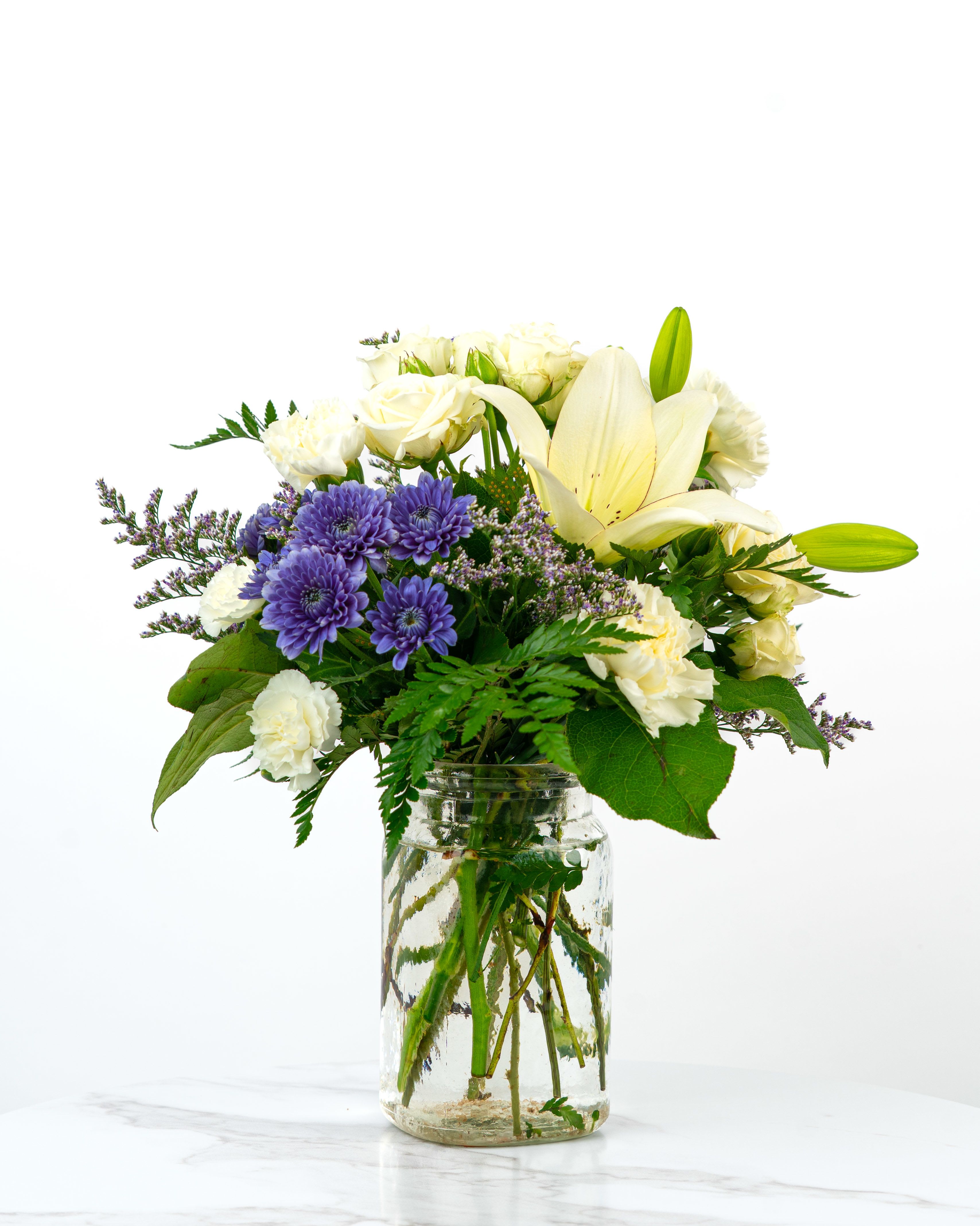 White lilies and purple daisies in a glass jar vase