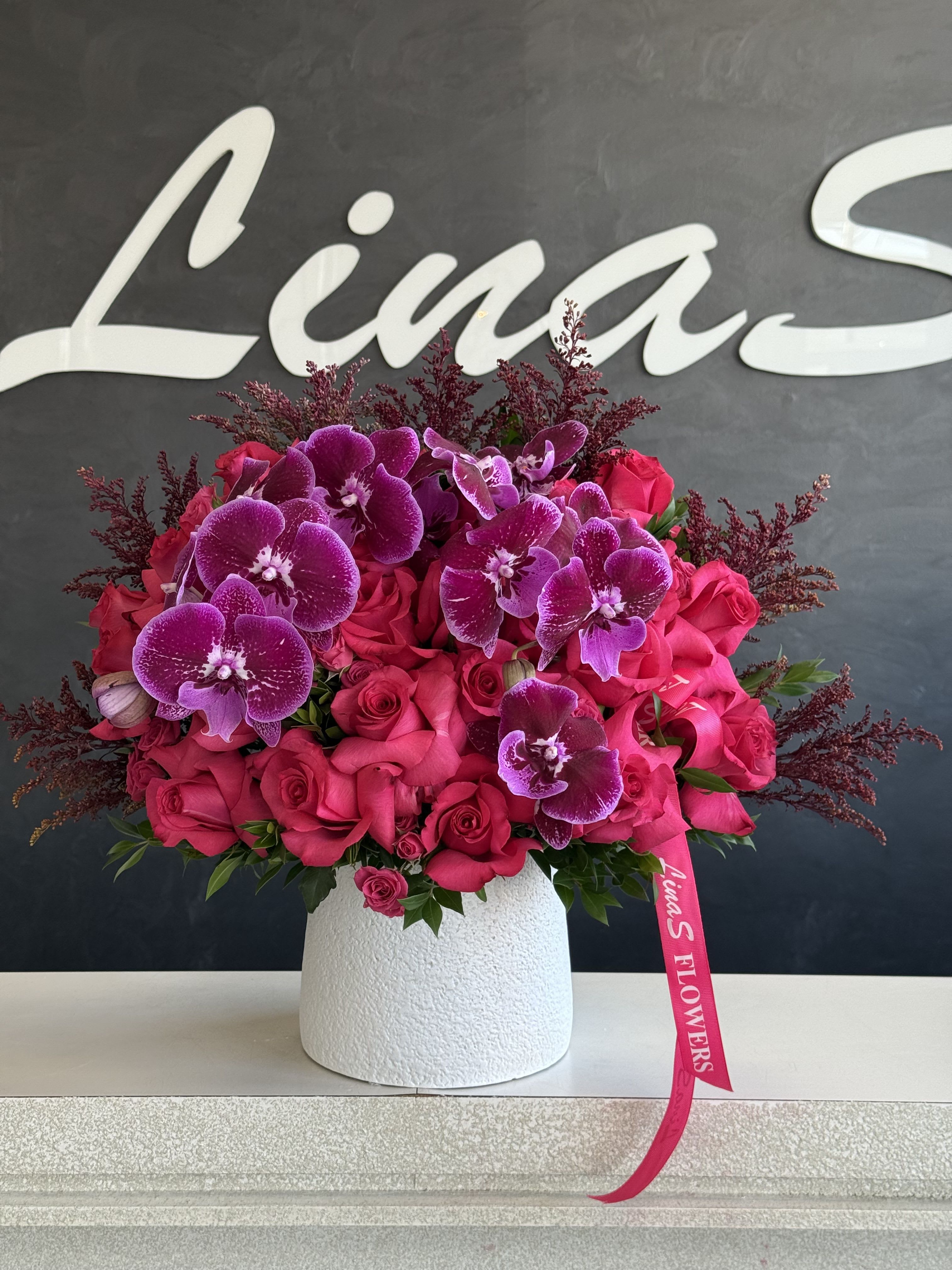 Pink roses and purple orchids arranged in a white vase