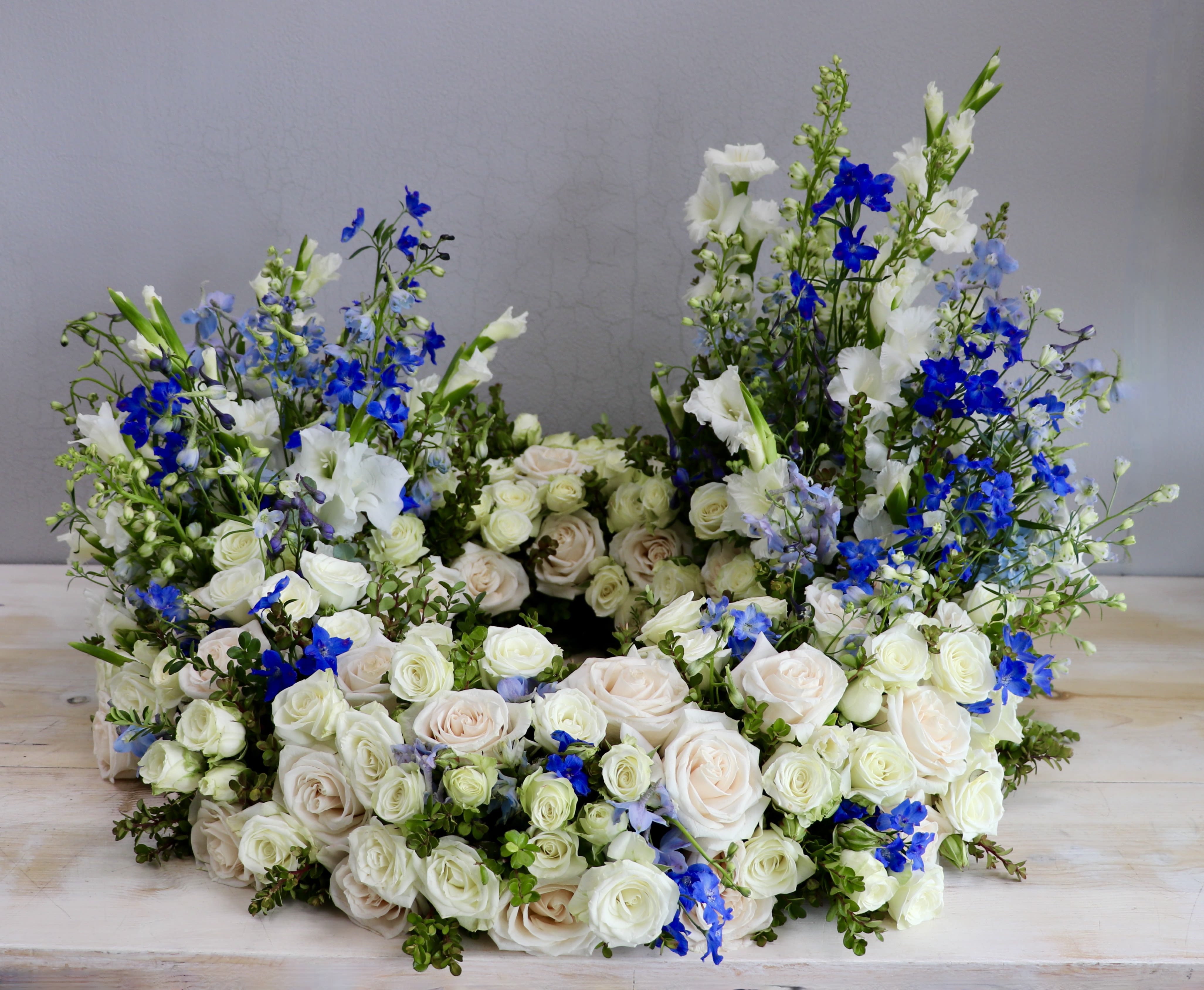 Urn Wreath in Blues  - This urn tribute wreath includes a mix of flowers, roses, and seasonal greens.     Standard size is 30'', deluxe is 36'' and premium is 42''. Interior diameter is about 10'' for standard size.