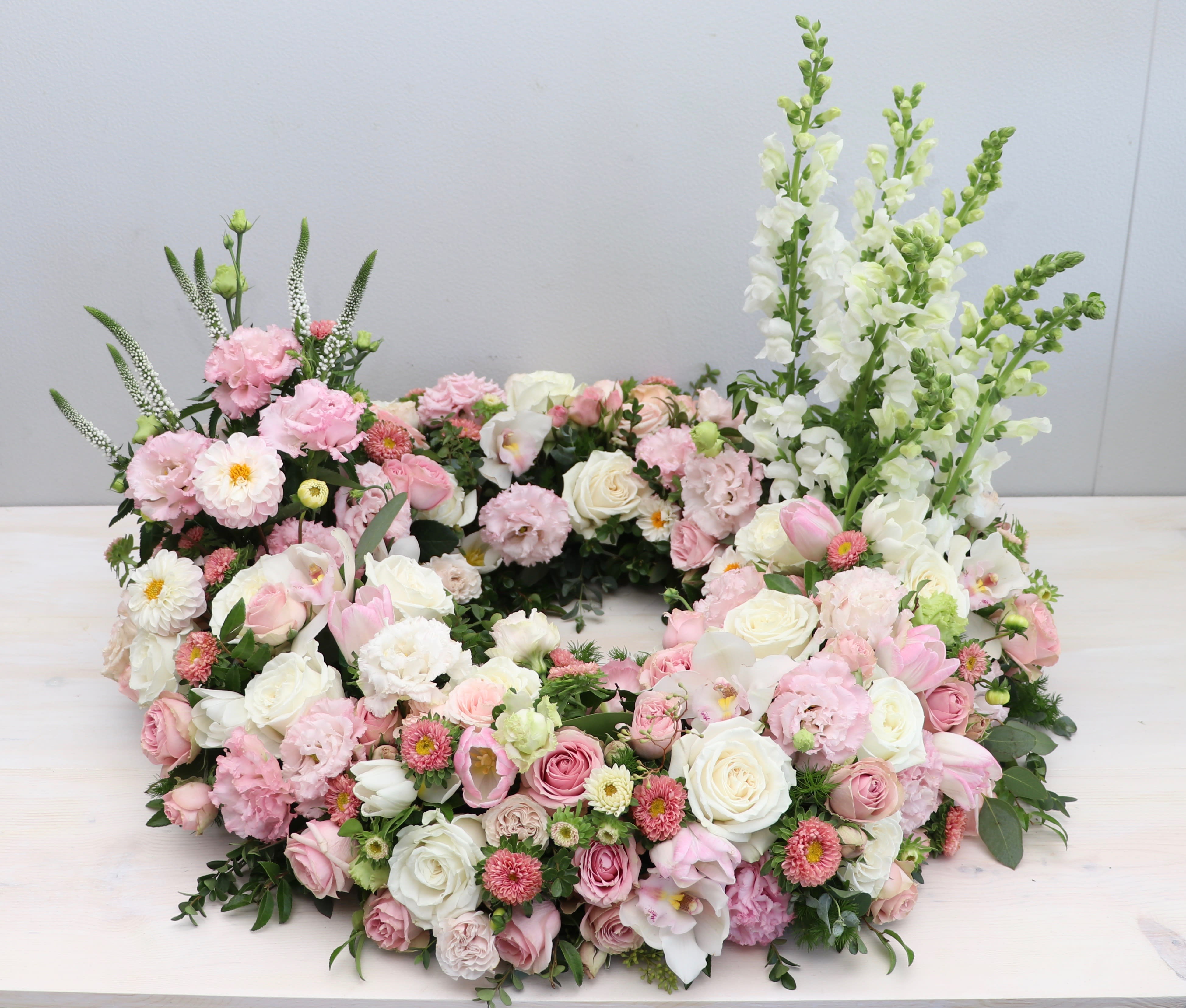 Urn Wreath in Pinks  - This urn tribute wreath includes a mix of  flowers, roses, and seasonal greens.     Standard size is 30'', deluxe is 36'' and premium is 42''. Interior diameter is about 10'' for standard size. 