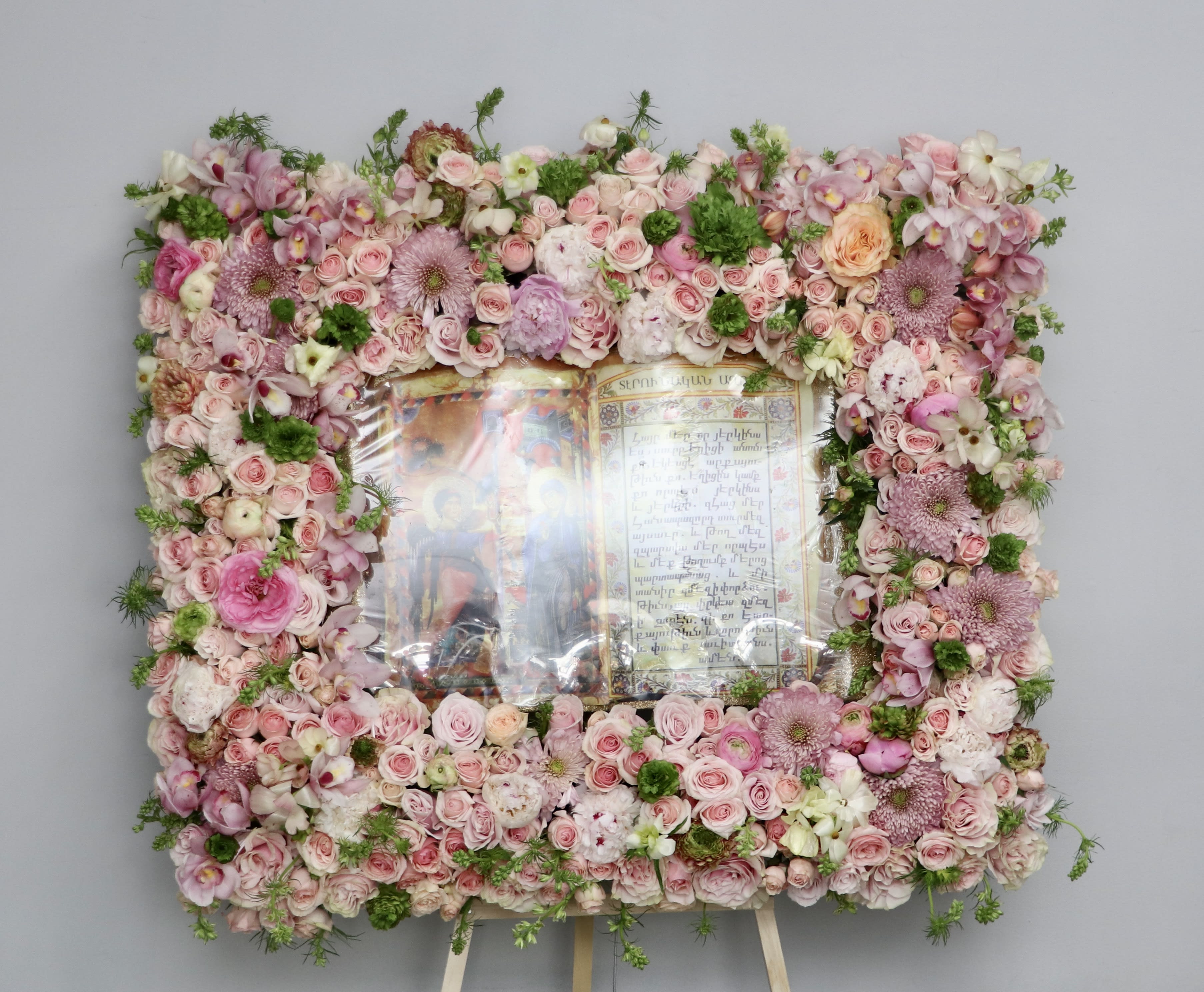 Pink Mixed Bible  - This frame includes pink roses and seasonal greenery. The standard size is approximately 36 inches tall and 24 inches wide. Additional flowers will be added for deluxe and premium sizes.    We include easel, printed banner, and delivery (some fees may apply). An additional banner can be added for $15.   