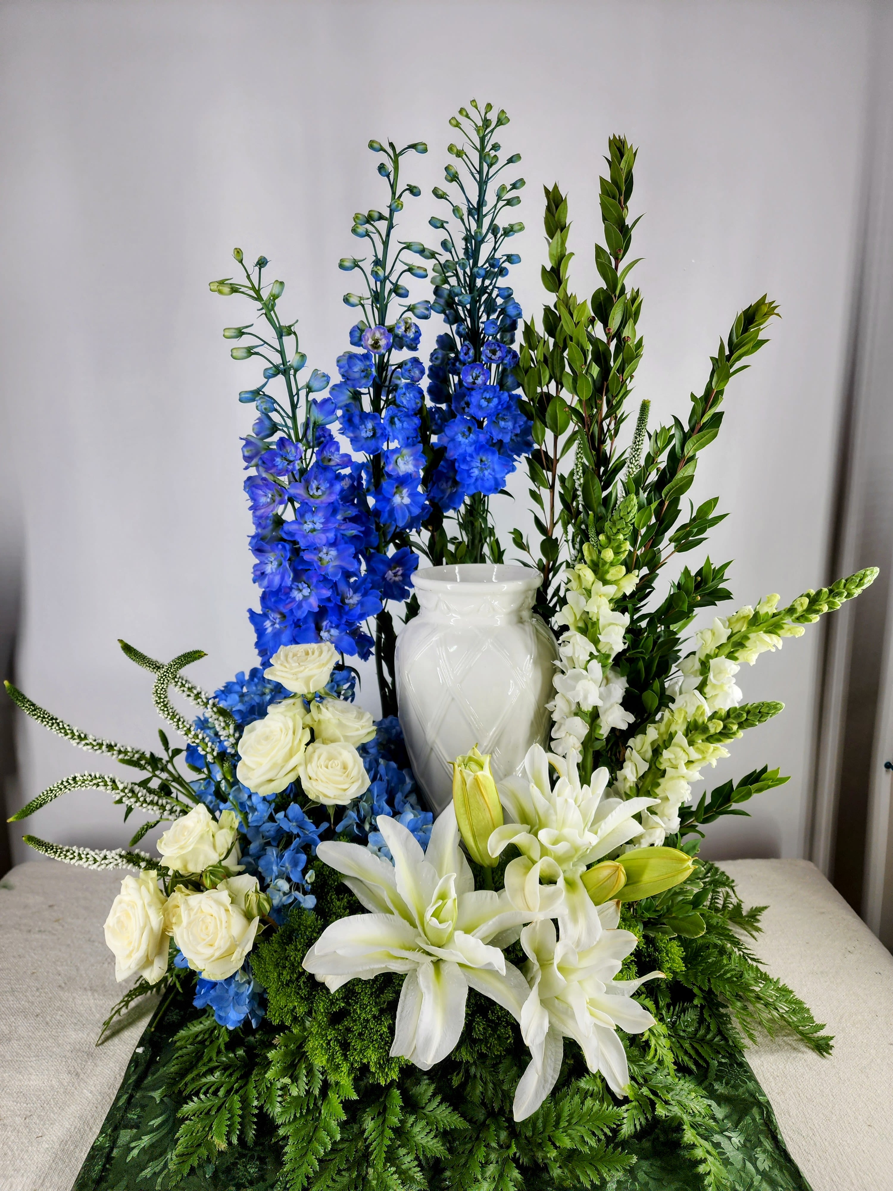 White lilies and roses with blue delphinium in a white vase