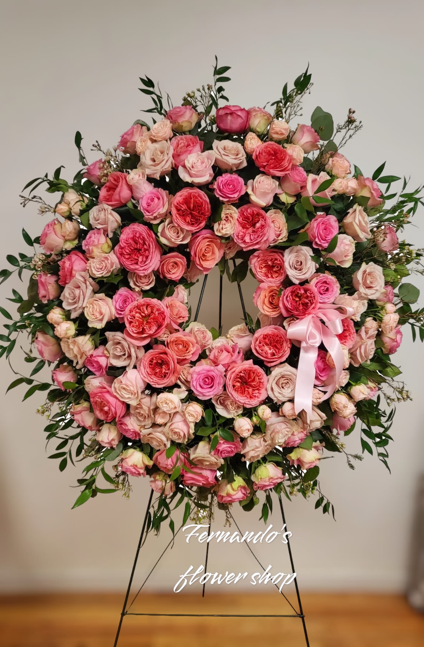 Large pink and peach rose wreath with satin bow displayed on a metal easel