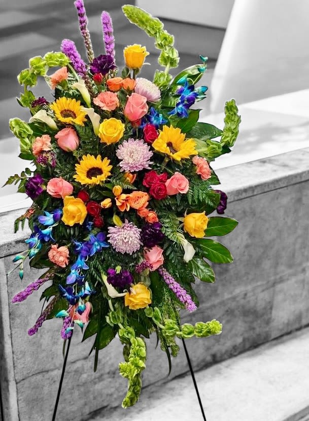 Tall multicolored standing spray with sunflowers, roses, orchids, and other blooms on a metal easel