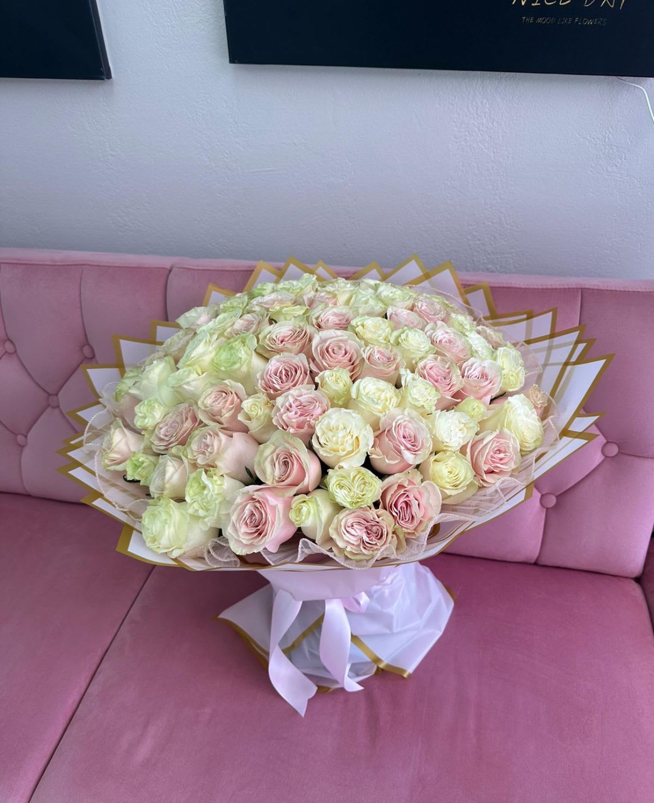 Large bouquet of pale pink and cream roses wrapped in white paper with gold trim