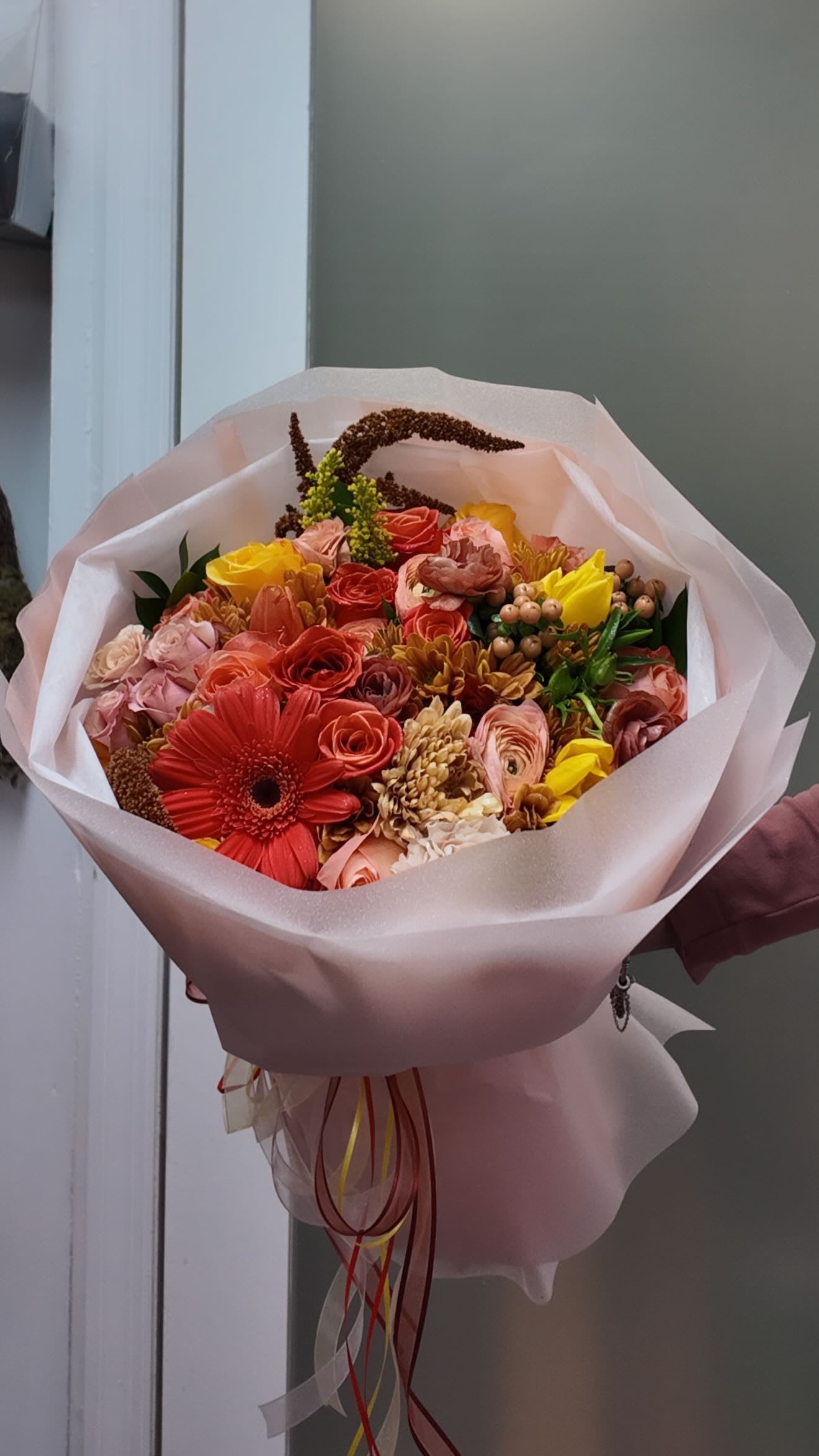 Bouquet of red, pink, and yellow flowers wrapped in pale pink paper