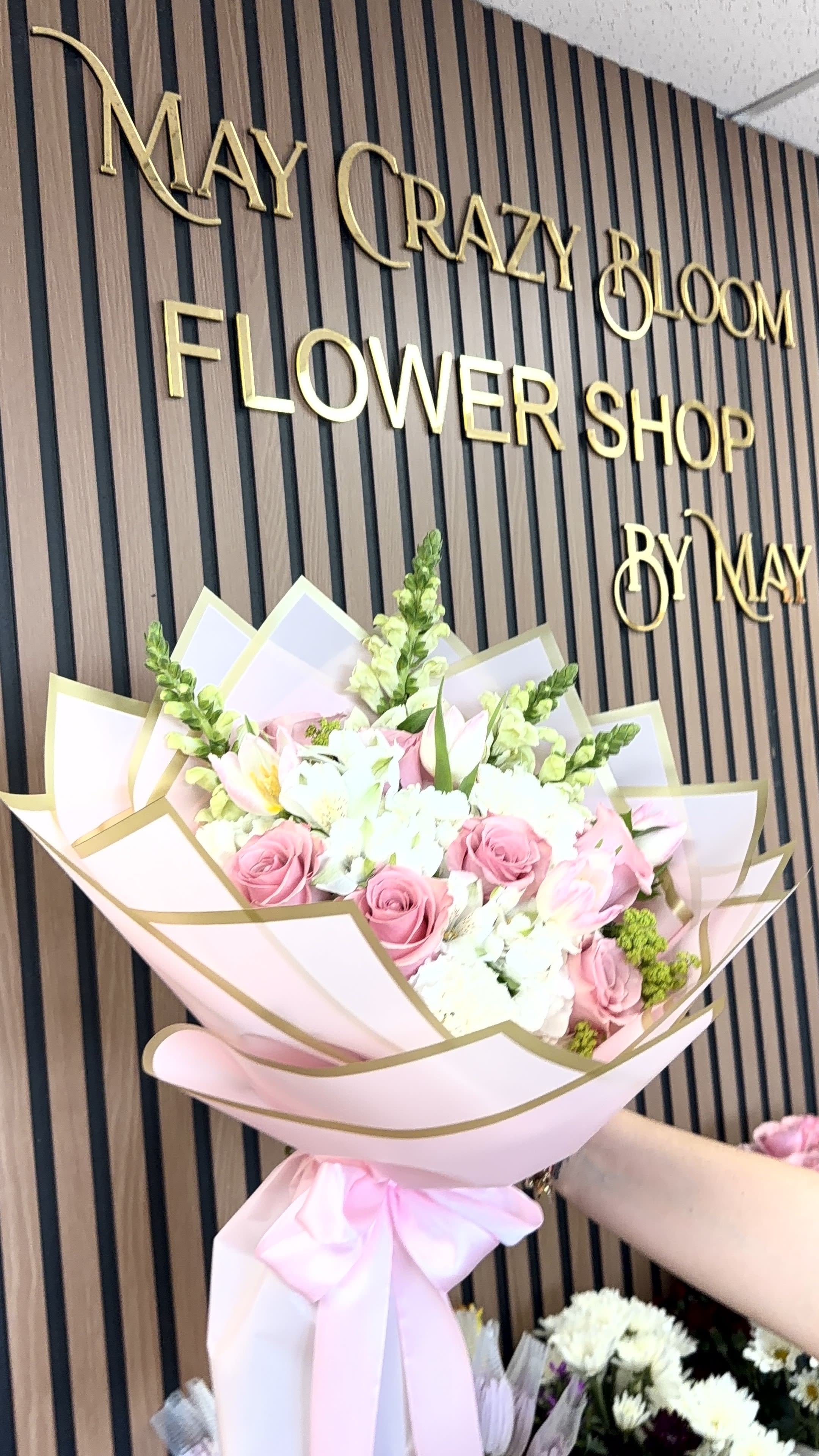 Petals  - Soft pink roses paired with delicate white alstroemeria and tall green snapdragon spikes create a romantic birthday bouquet that feels both fresh and feminine. Perfect for anniversaries, Mother's Day, or simply to make someone's day, this arrangement reads as gentle and layered-she'll feel seen and celebrated the moment she unwraps it.  The arrangement is wrapped in pastel pink paper with a gold-edged outer wrap and tied with a large pink ribbon for a polished, gift-ready presentation. Textures move from velvety rose petals to the airy vertical lines of snapdragons and the speckled charm of alstroemeria, giving the bouquet depth and a light, uplifting silhouette.  This is the kind of everyday-luxury bouquet that works for mothers, partners, or friends who appreciate soft, romantic colorways. Order with same-day pickup or delivery where available; trim stems and refresh water on arrival to keep blooms looking their best.