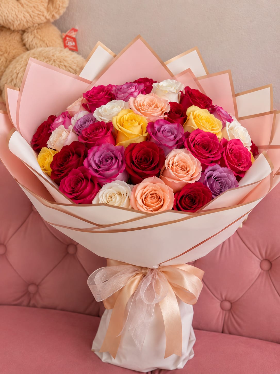 100 Wrap of roses - A lush, full dome of one hundred roses in a joyful palette of pink, white, yellow, purple and warm peach-orange - a grand birthday bouquet, anniversary roses, or wedding gift that reads as both celebratory and effortlessly romantic. The sheer abundance of blooms creates a soft, petal-rich texture that makes the recipient feel deeply cherished the moment they see it.  Each bloom is tightly packed into a rounded arrangement wrapped in crisp white paper and tied with a simple ribbon for an upscale presentation that keeps the focus on color and volume. This large bouquet is perfect for marking major milestones or surprising someone who deserves something unforgettable; it arrives ready to display and will keep its fresh, fragrant presence for days with fresh water and routine stem recutting.