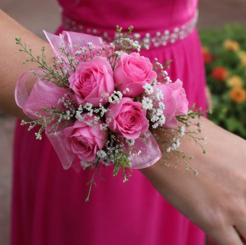 Simple Hot Pink Corsage  - Bright clusters of bright pink spray roses make a romantic statement in this wrist corsage-perfect as a prom corsage or a wedding accessory for bridesmaids. The compact, wrist-style arrangement reads feminine and celebratory, sending a clear message of affection and festivity to the person you're honoring.  Tightly grouped pink roses are accented with small white filler flowers and airy green sprigs for a light, textured look. A sheer pink ribbon wraps the base for secure, comfortable wear and adds a soft, formal finish. Sized to sit neatly on the wrist, this corsage pairs beautifully with strapless dresses, updos, or a simple boutonniere to complete a coordinated look; gentle misting and cool storage will keep the flowers fresh through the event.