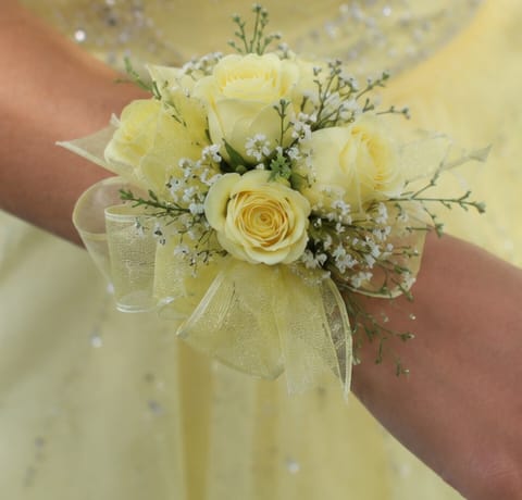 Simple Yellow Spray Rose Corsage  - Pale yellow spray roses clustered into a compact wrist corsage make a soft, romantic statement for a wedding or prom. This wrist corsage for spring or summer events pairs the delicate yellow roses with small white filler blooms and airy green sprigs, so the person you're honoring will feel celebrated and gracefully styled for the occasion.  Hand-tied on a comfortable wrist corsage band, the arrangement is finished with translucent yellow sheer ribbon for a formal yet effortless look. The petite scale keeps it elegant and wearable during photos and dancing; colors are pale yellow, white, and green. Ideal for bridesmaids, prom dates, or anyone you want to mark with a gentle, classic floral touch.