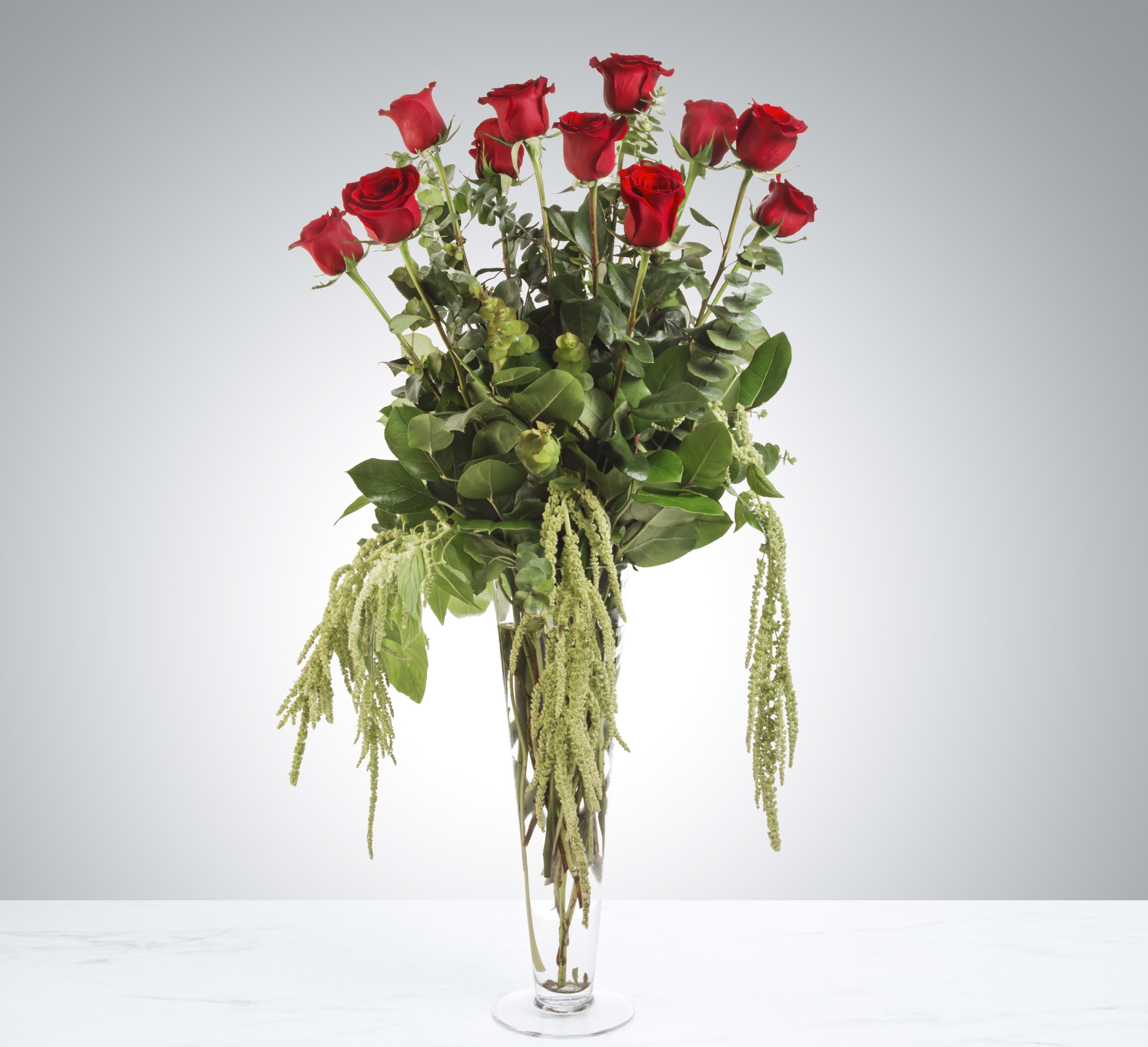 Tall bouquet of red roses in a clear glass vase with trailing greenery