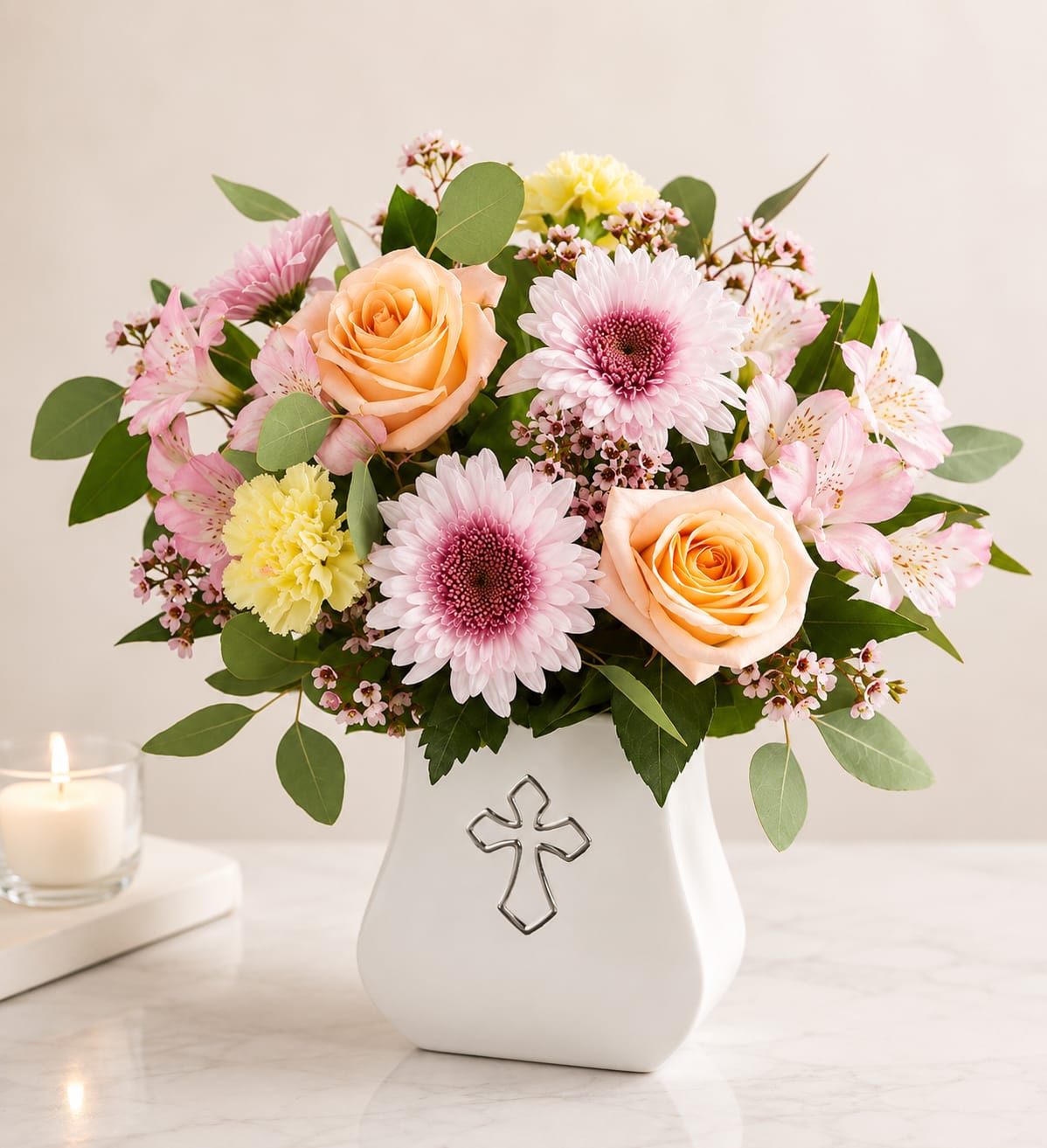 Gentle Grace Bouquet - Express your heartfelt sympathy with this elegant arrangement featuring soft peach roses, pink gerbera daisies, delicate alstroemeria, carnations, wax flower, and fresh greenery, beautifully arranged in a keepsake ceramic cross vase. A thoughtful tribute that offers comfort, peace, and loving remembrance during life's most difficult moments.