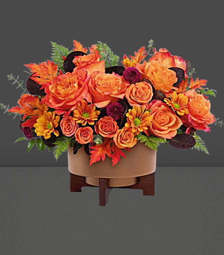 Orange roses and autumn flowers in a round container