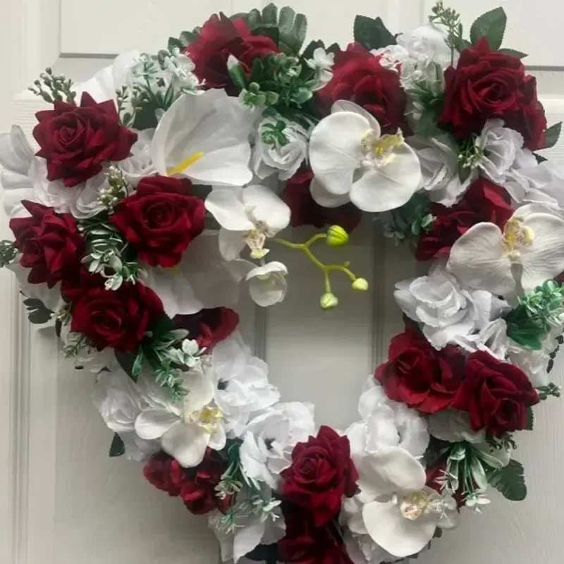 memorial wreath x69 - A heart-shaped sympathy wreath that speaks in classic red and white, designed to honor a loved one with timeless elegance. This memorial wreath for funerals and remembrance features deep red roses and pristine white Phalaenopsis orchids arranged in a dense, layered heart silhouette-an immediate, heartfelt statement that will make the person you're remembering feel visibly cherished.  The arrangement rests on a wreath form and is tightly clustered so the rich red roses form a bold outline while the glossy white orchids and small white accent blooms provide luminous contrast. Green foliage peeks through to give depth and a natural frame, and the overall finish is polished and formal-suitable for a chapel, graveside, or memorial display.  Made to convey sympathy and enduring love, this heart wreath is appropriate for family tributes, partner memorials, or to mark an anniversary of passing. Designed for immediate display on arrival; minimal care is needed-keep sheltered from direct sun and wind to preserve blooms during the service.