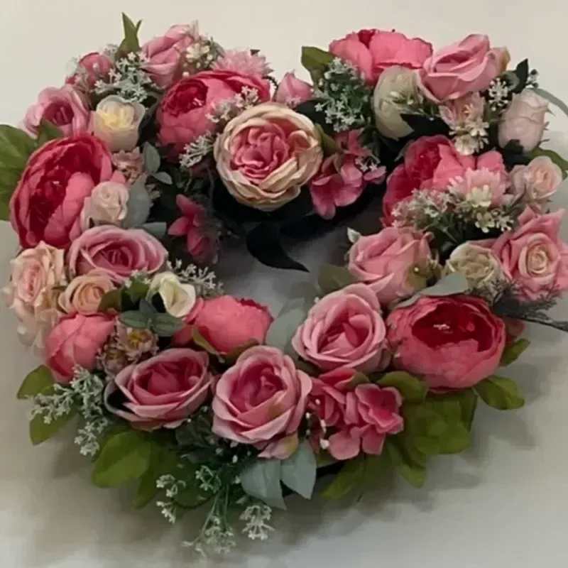 Memorial Wreath X25 - Tightly clustered pink and red roses form a heart-shaped wreath that speaks of lasting love and remembrance-an elegant sympathy and funeral arrangement designed to comfort and honor. The heart-shaped wreath form gives this floral tribute a clear, affectionate silhouette that makes it ideal for saying goodbye to someone dear or for sending condolences to a grieving family.  Layers of blush-pink and deeper red roses are interspersed with small white filler blooms and green foliage that peeks around the edges to define the heart. The design is full and rounded, with soft petal textures and a layered look that reads both romantic and respectfully celebratory. Handcrafted on a heart-shaped wreath form, this piece presents a clean outline and a lush surface of blooms for a polished, enduring display.  Choose this wreath to express love, sympathy, or heartfelt remembrance at a funeral service or graveside gathering-the kind of floral tribute that helps the recipient feel seen and supported. Standard care for wired and foam-mounted wreaths applies: keep cool, avoid direct sun, and place on an easel or flat surface as directed when delivering to a service.
