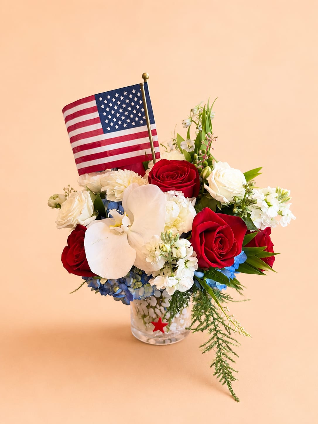 Stars &amp; Blooms - Celebrate the spirit of Independence Day with "Stars &amp; Blooms", a timeless arrangement featuring vibrant red roses, crisp white blooms, and shocking blue hydrangea. Designed in a keepsake vase, this elegant centerpiece brings patriotic charm and fresh beauty to holiday gatherings, backyard celebrations, or as a thoughtful gift to honor those who serve. Perfect for celebrating freedom with style and grace!