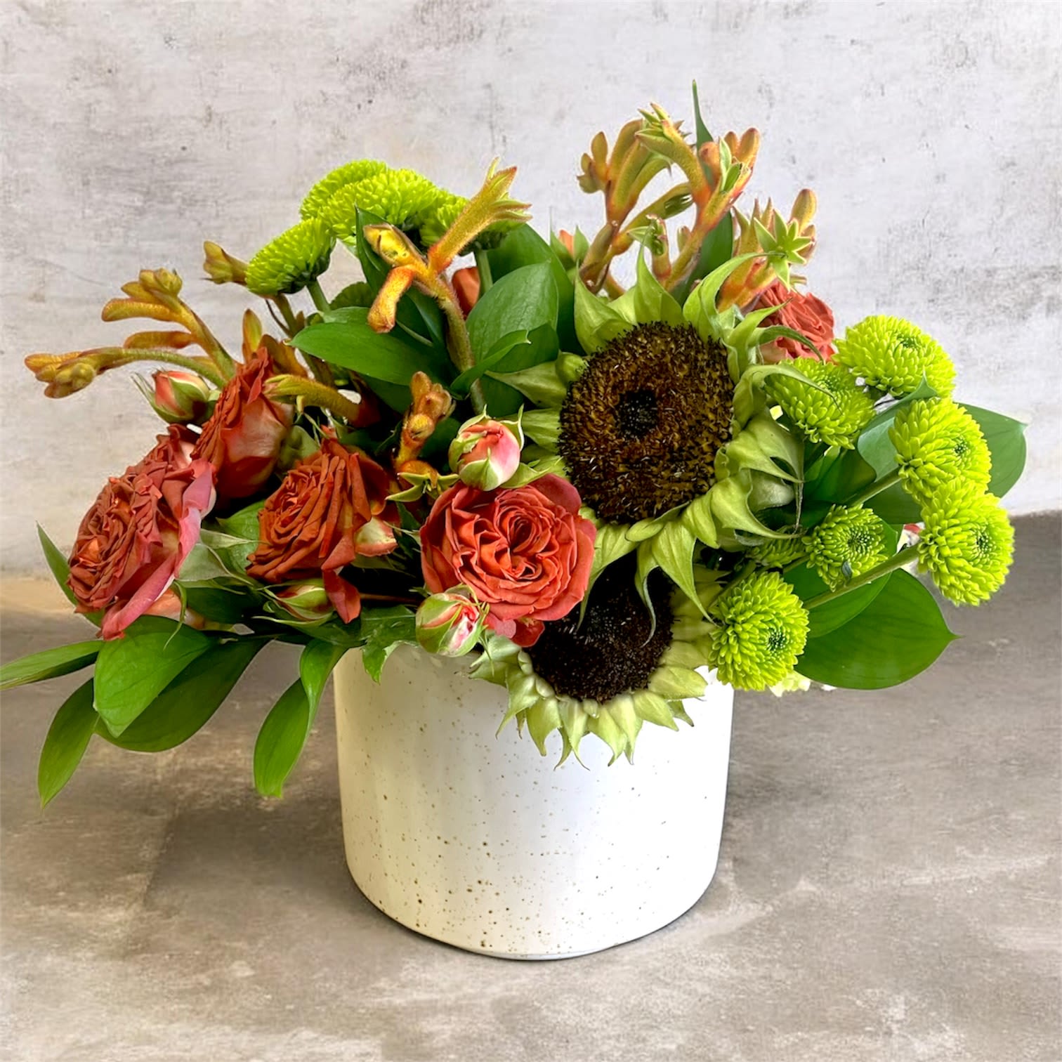 Redwood - Rust-orange roses, kangaroo paw, naked sunflowers, and green button chrysanthemums in a low ceramic vase creates a warm, textural arrangement that transports you to a forest filled with redwood trees and soothing energy.