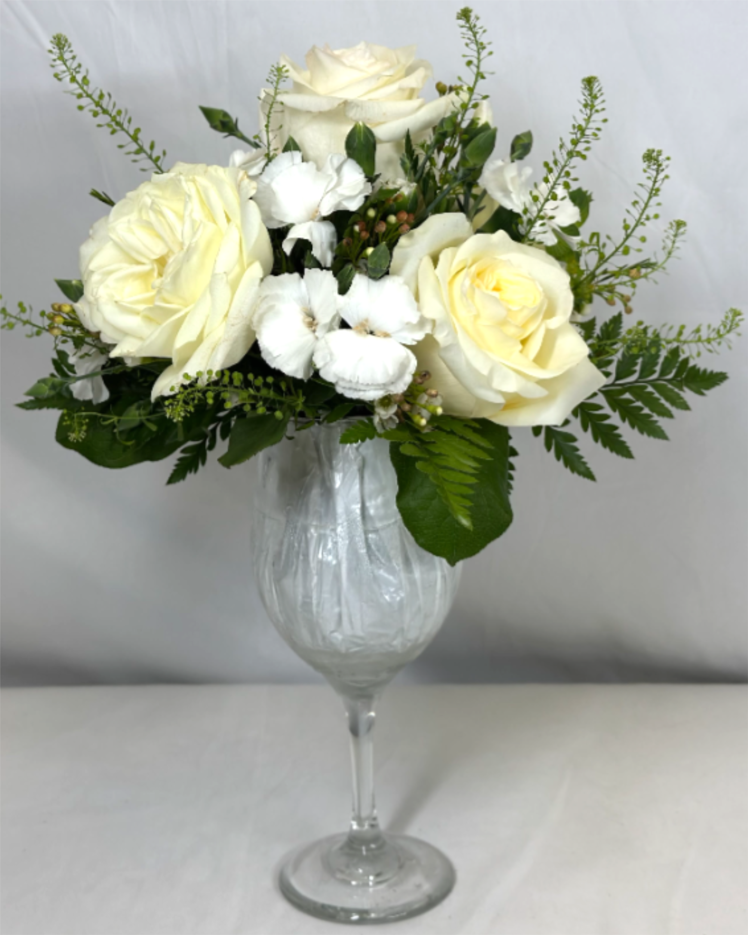 Raise a Glass! White Wine - What better way to celebrate than with flowers and wine!? We will take care of the flowers with this beautiful arrangement in white and ivory, designed in a large sturdy reusable wine glass. You supply the wine, and it will bring a smile for all. If the featured flowers are unavailable we will create your gift using the freshest available blooms of equal or greater value.