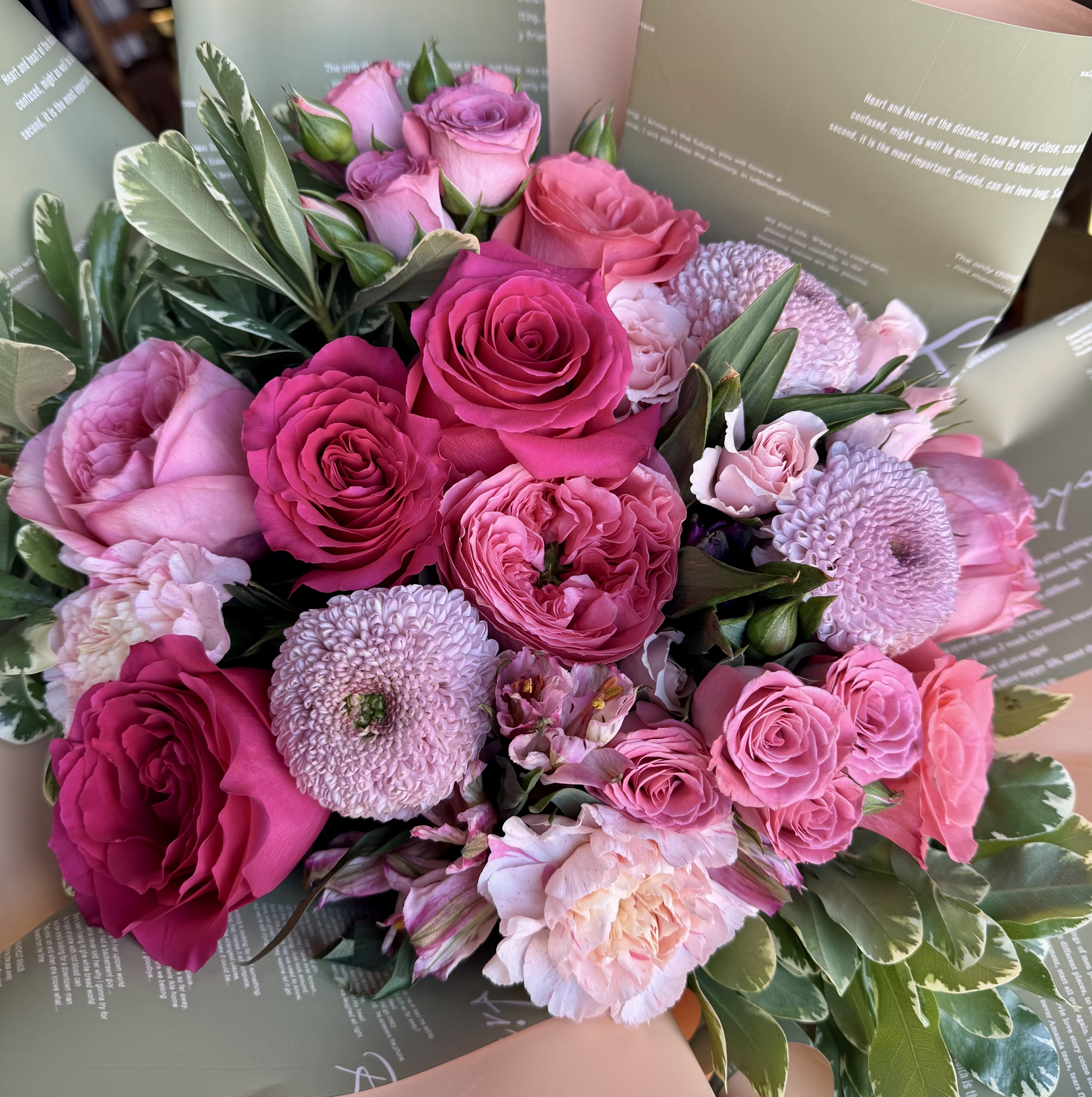Affection flower Bouquet - Indulge in a lush tapestry of pinks and deep berries. This hand-tied bouquet is a masterclass in texture, featuring velvety Premium Roses and delicate Spray Roses nestled alongside geometric Pompon Chrysanthemums.  Accented with ruffled Carnations and framed by variegated Pittosporum greenery, this arrangement offers a garden-fresh aesthetic. 