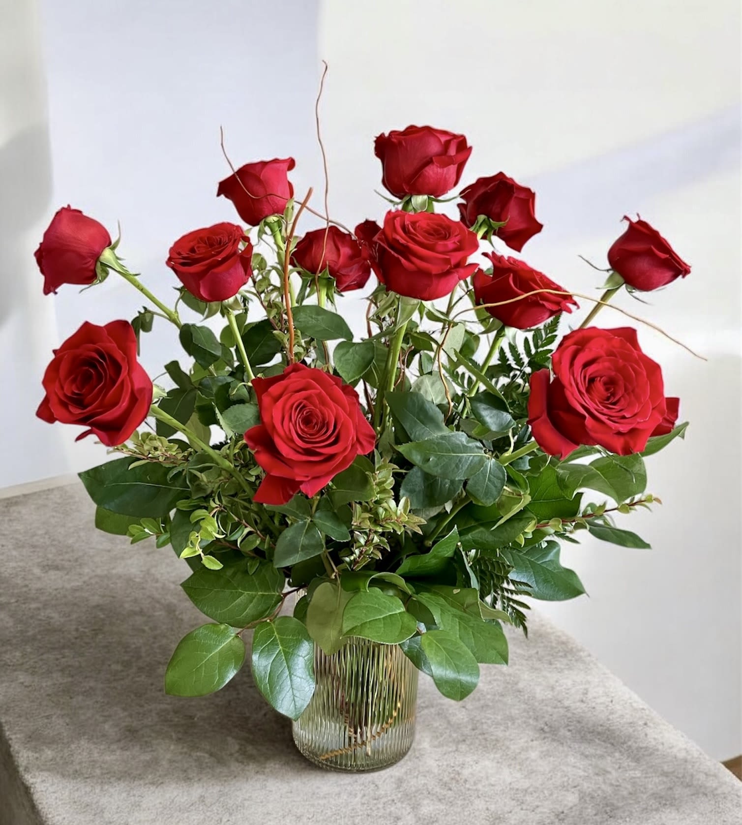 Simply Red - A timeless and dramatic arrangement featuring stunning red roses, artfully accented with fresh seasonal greenery. Pictured as Standard, 12 stems. Deluxe is 18 stems, Premium is 24 stems.
