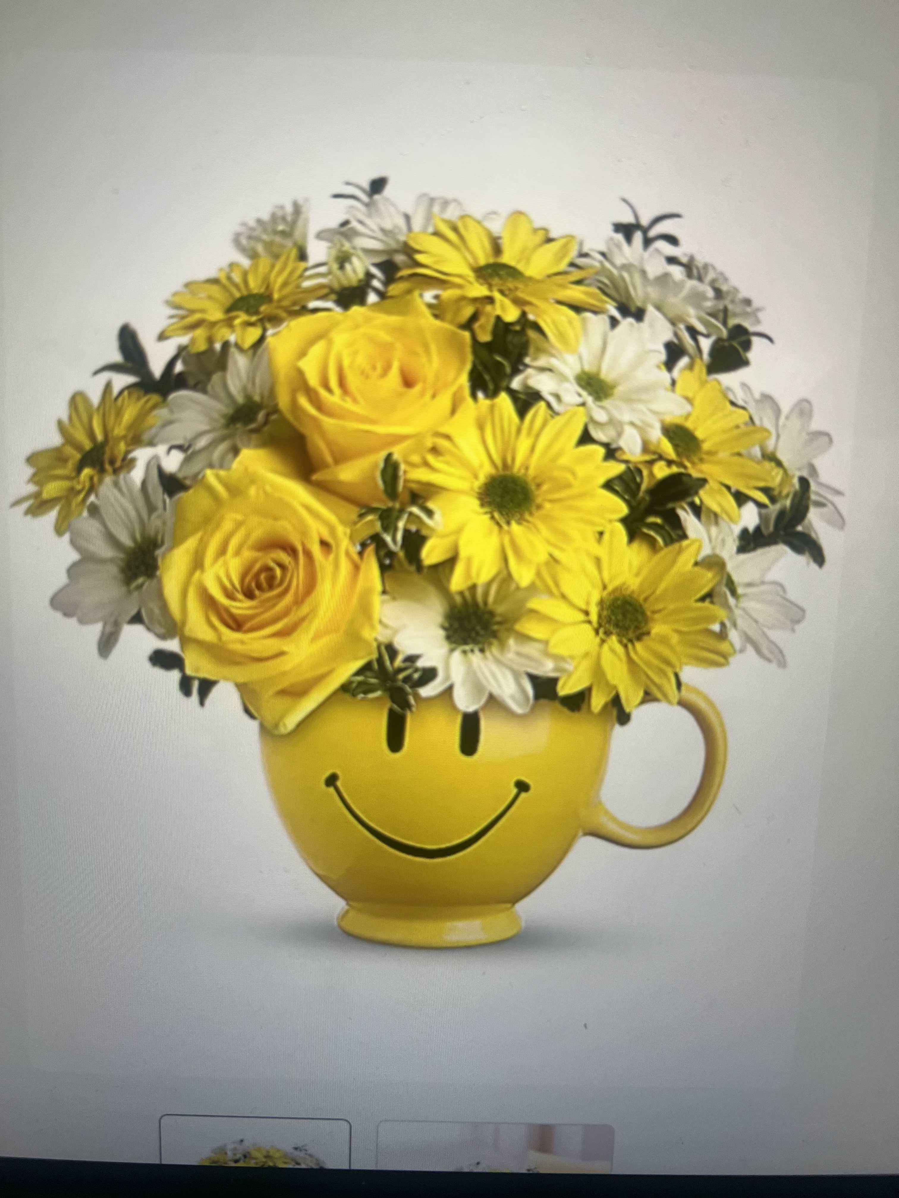 Birthday Smiley Face - Sunshine in a mug - bright yellow roses and cheerful white-and-yellow daisies are arranged low and full in a yellow ceramic mug printed with a smiley face, making this birthday bouquet perfect for a birthday, congratulations, or just-because surprise. The playful, rounded silhouette and saturated yellow-and-white palette read as instantly upbeat; the person you're thinking of will feel noticed, uplifted, and celebrated the moment they see it.  The compact arrangement sits wide over the mug, packed densely for a full, textured look that balances the soft rose petals with the daisy's sunny centers and fresh greenery. The ceramic mug doubles as a keepsake container, ready for reuse on a desk or kitchen counter when the flowers fade.  Ideal for friends, coworkers, or anyone who prefers casual, joyful gifts, this piece arrives ready to display with simple care: keep water fresh and trim stems every few days to extend bloom life. The mug makes wrapping optional and turns the bouquet into a ready-to-gift item that says "happy day" in a bright, friendly way.
