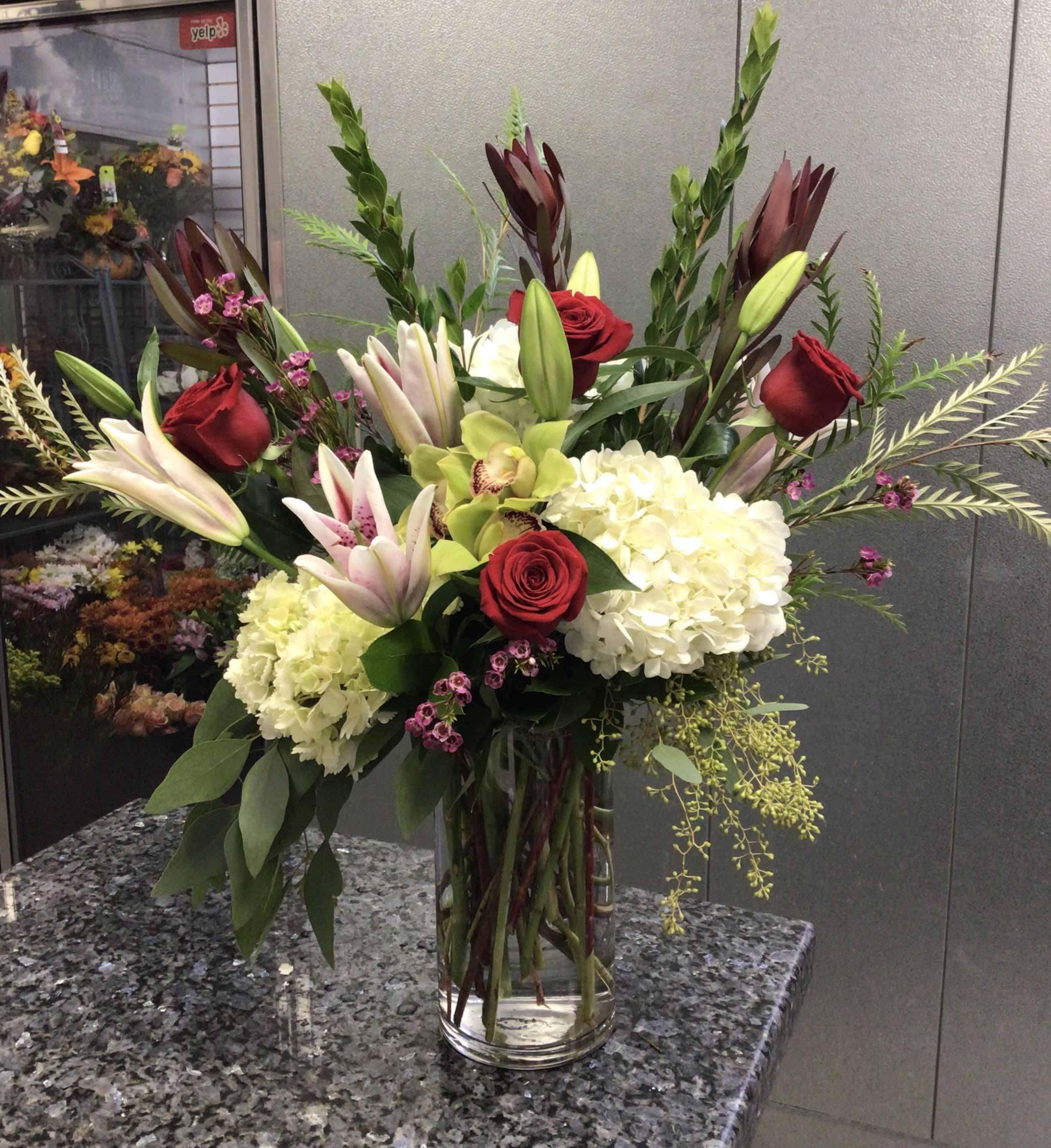 Tall bouquet of red roses, lilies, and white hydrangeas in a glass vase