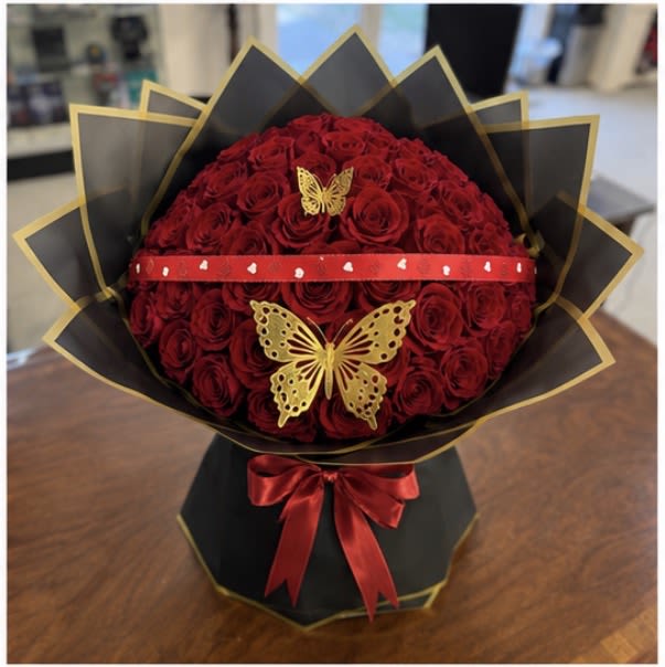 Ramos Buchones - 50 Rose Bouquet - Bouquet Details:  * 50 premium fresh red roses * Elegant black wrap with gold trim * Decorative heart-accent ribbon * Gold butterfly embellishments * Handcrafted in a modern, luxurious presentation * Approximate bouquet diameter: 18–20 inches  Whether celebrating a milestone or sharing a heartfelt gesture, the 50 Red Rose Signature Bouquet is a timeless expression of love, passion, and elegance.