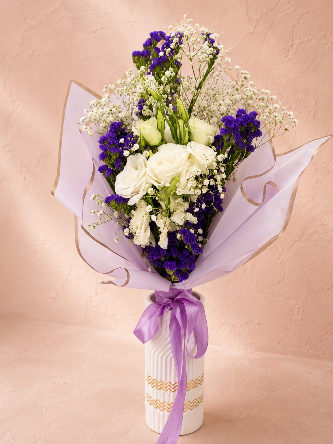 Eir's Moonlit Grace Vase Bouquet - Inspired by Eir, the Norse goddess of healing and compassion, this bouquet reflects serenity, grace, and timeless elegance through its luminous palette of white blooms and delicate violet accents.  Designed in Flower Fairy's signature garden style, this luxury wrapped bouquet features premium white roses, elegant white lisianthus, rich purple statice, airy baby's breath, and fresh greenery. The soft contrast of crisp white and vibrant violet creates a refined composition with graceful texture and natural movement. Wrapped in premium lavender waterproof paper and finished with a satin ribbon, this bouquet offers a sophisticated expression of love, appreciation, comfort, and celebration.  Perfect for birthdays, anniversaries, thank-you gifts, sympathy, get well wishes, congratulations, or simply letting someone know they are in your thoughts.  Each arrangement is handcrafted by Flower Fairy using the freshest flowers available. While occasional substitutions may be necessary due to seasonal availability, we always preserve the overall style, color palette, and premium quality of every design.  Features: Premium white roses White/purple lisianthus Purple statice Baby's breath Luxury wrapped bouquet Waterproof designer wrapping Satin ribbon finish Handcrafted by Flower Fairy Same-day flower delivery in Phoenix