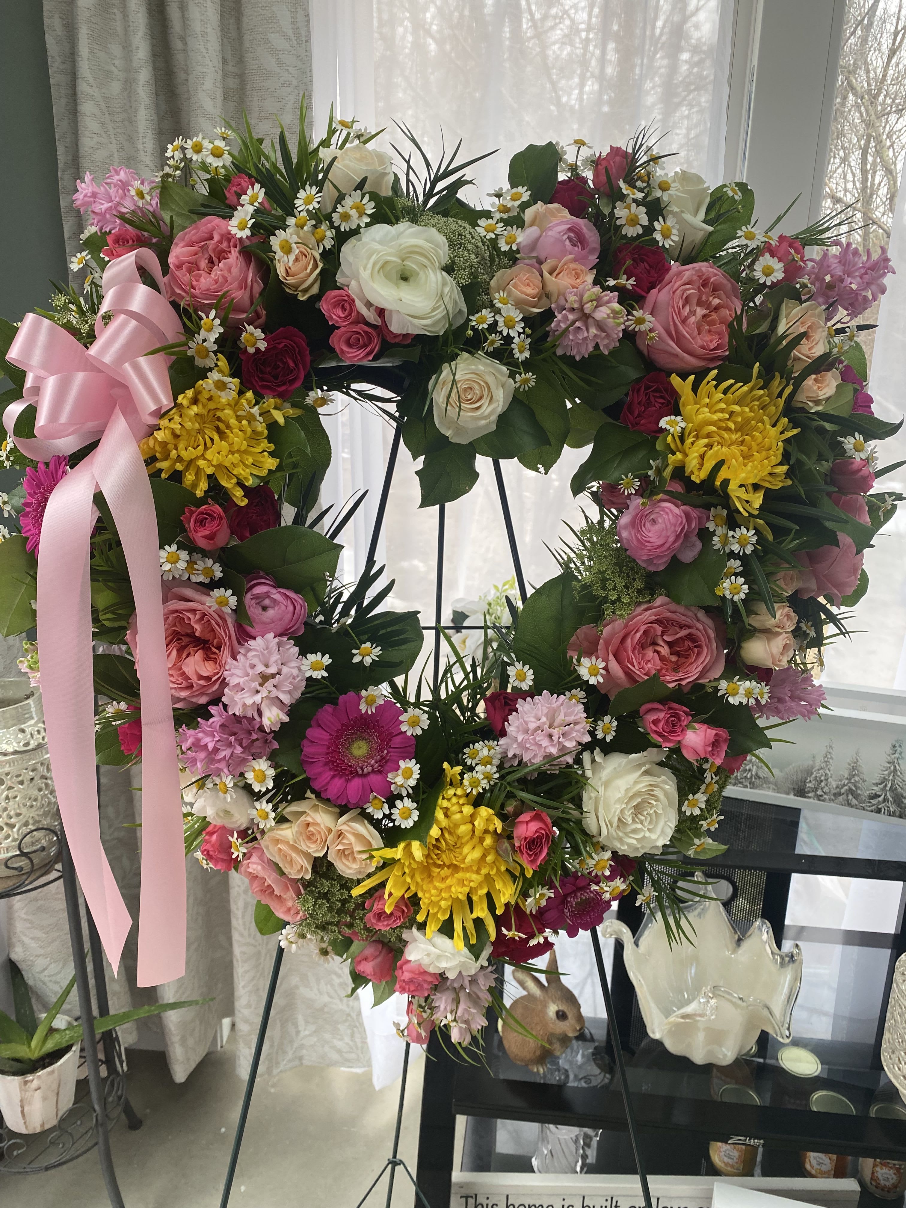 Heart-shaped floral wreath with pink, white, and yellow flowers on an easel
