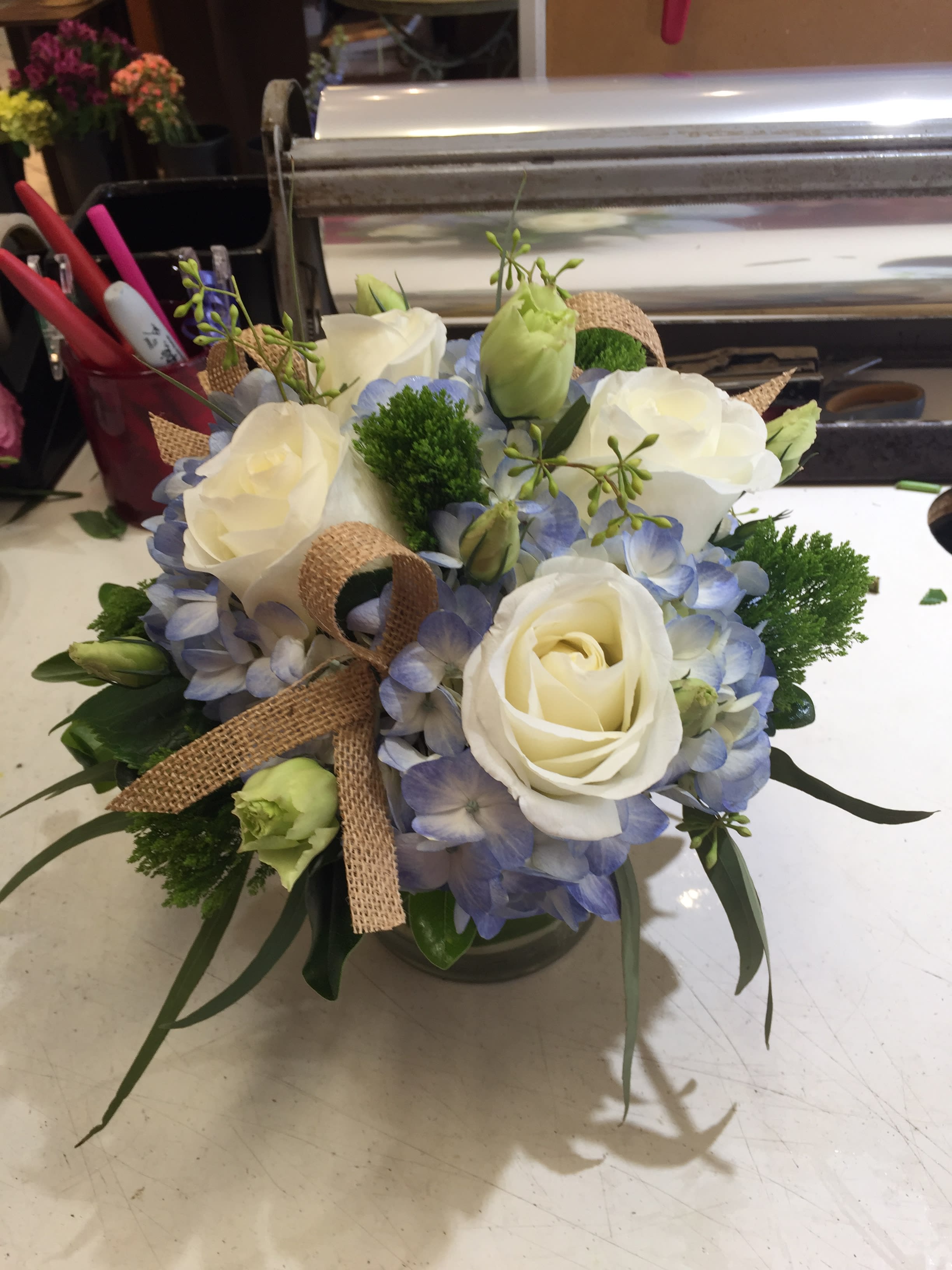 White roses and blue hydrangeas in a glass vase with burlap ribbon