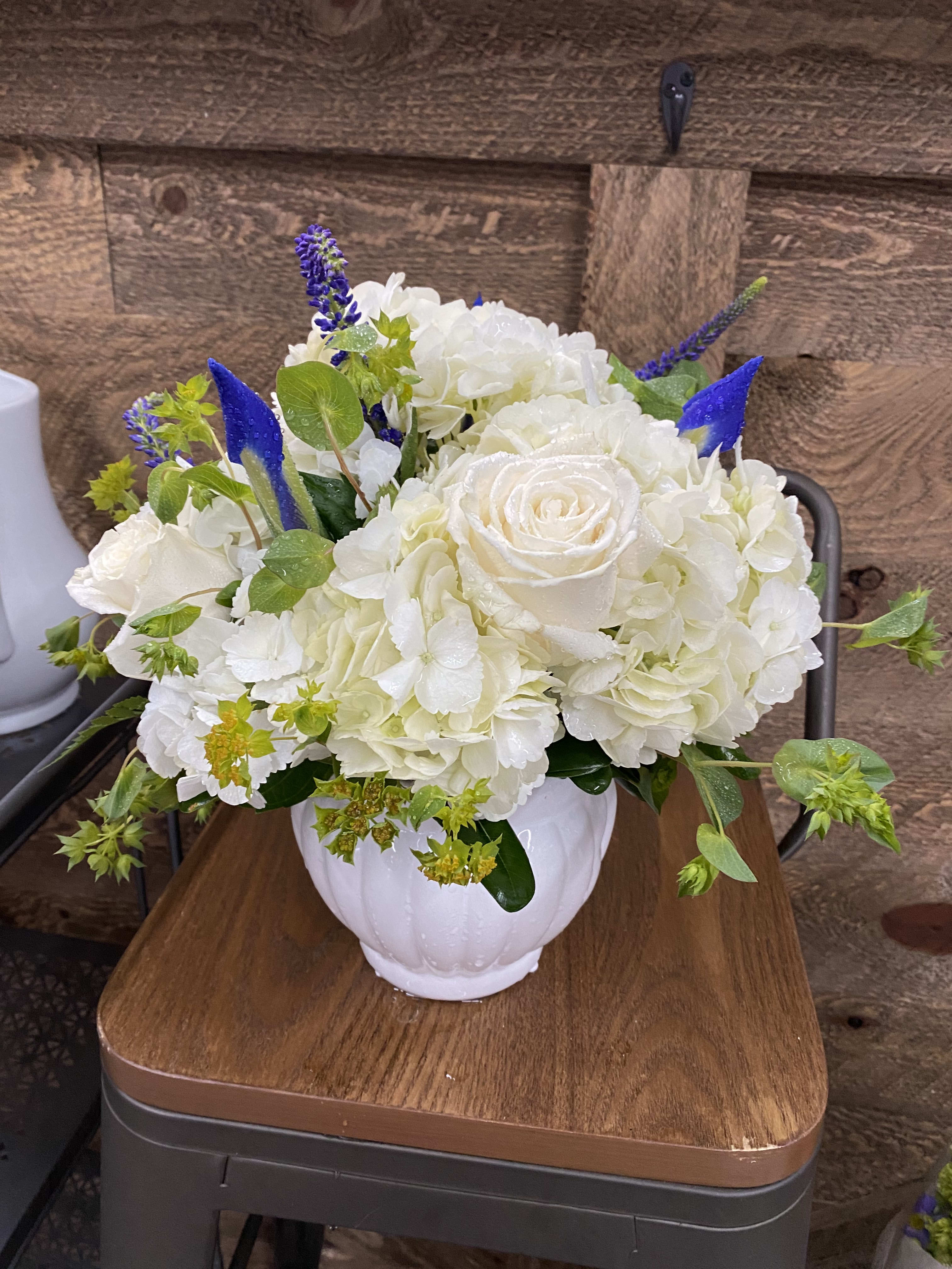 White roses and hydrangeas in a white vase with blue accents