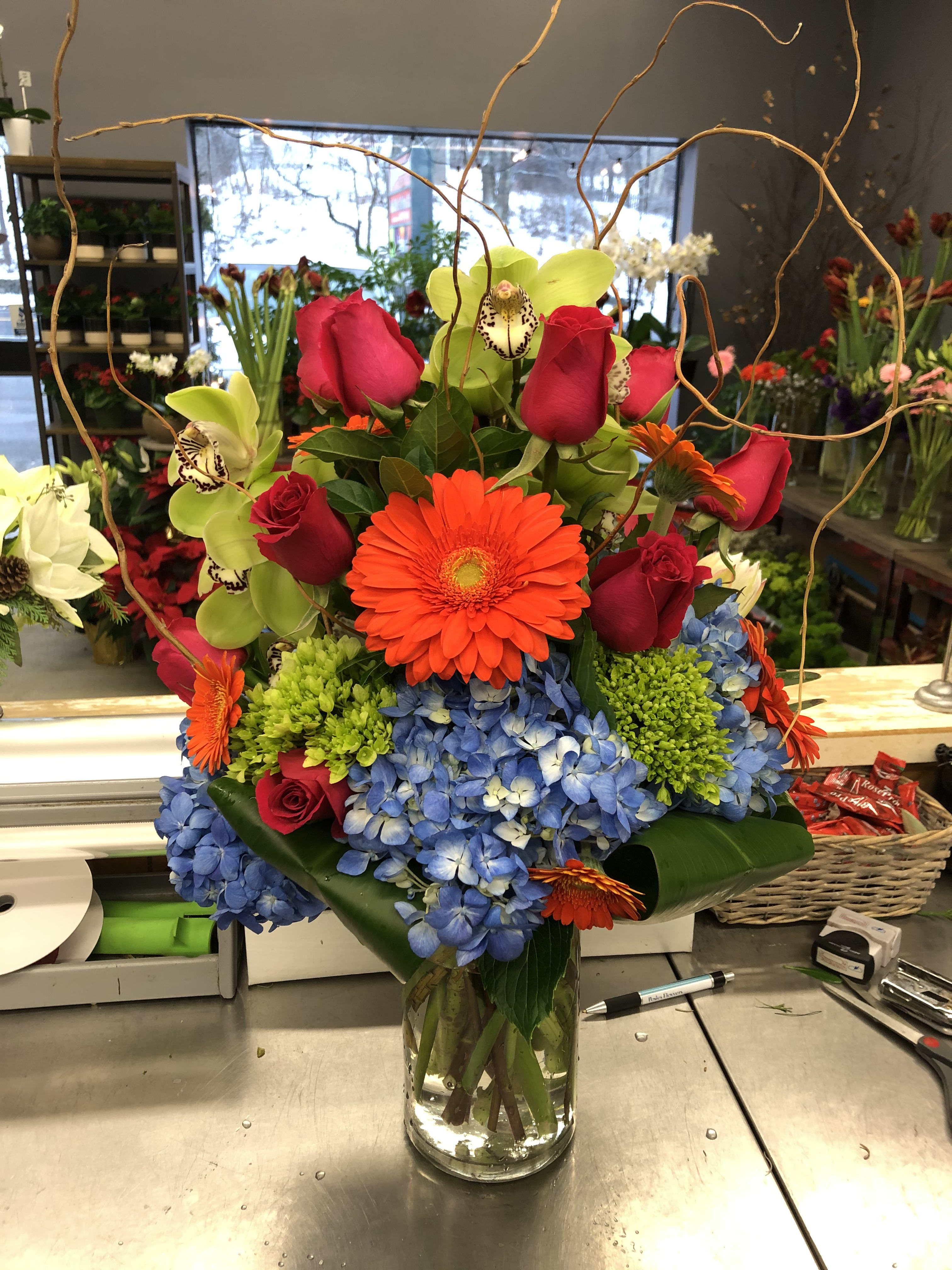Bright mixed bouquet in a glass vase with roses, orchids, gerbera daisies, and hydrangeas