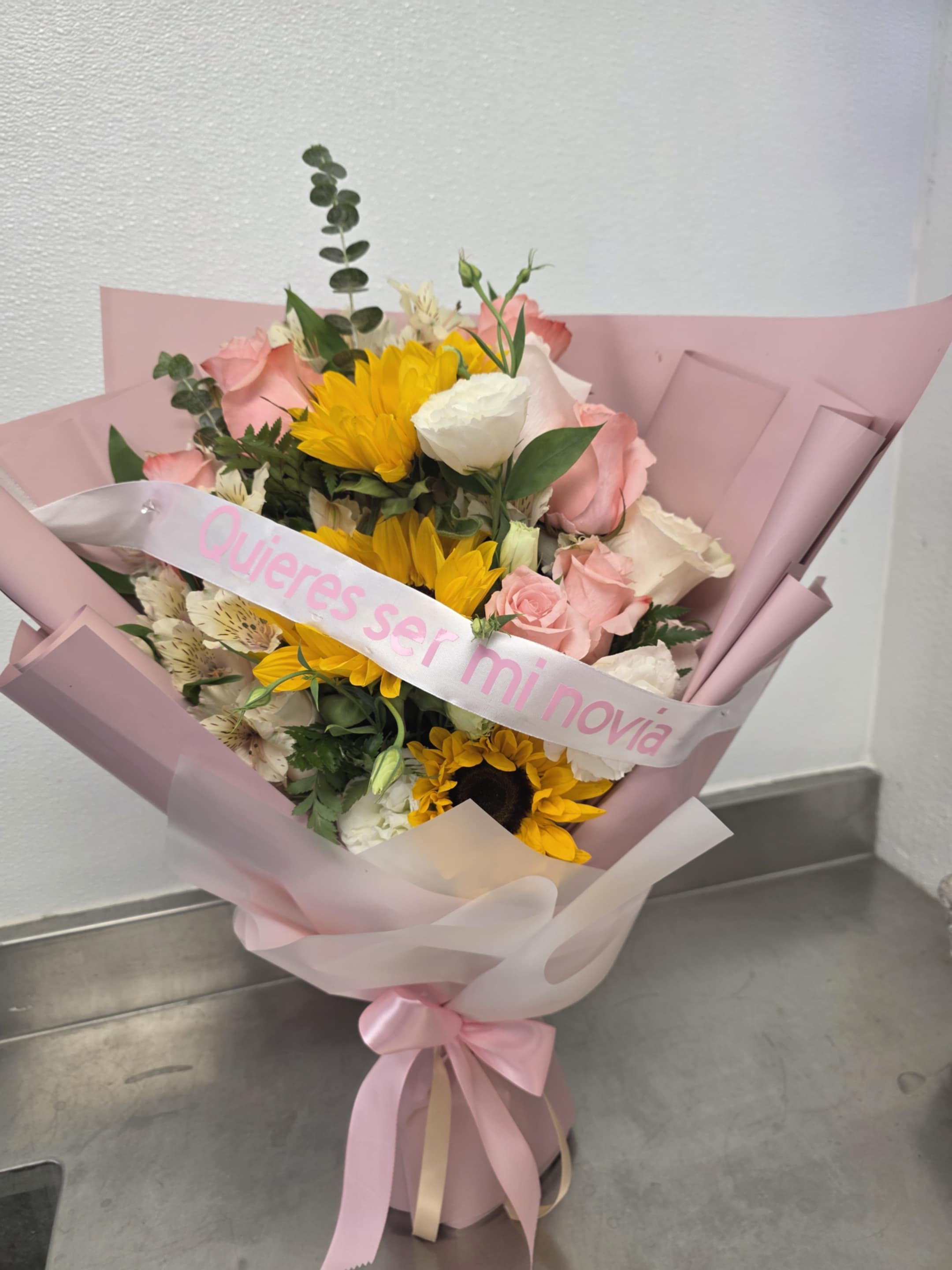Pink-wrapped bouquet with sunflowers, pink roses, and a white ribbon