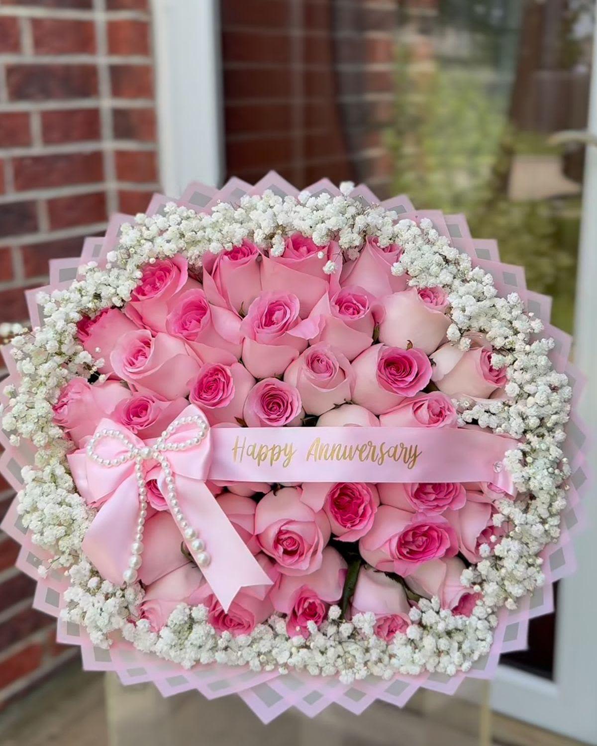 Bouquet de rosas C By Special Moment´S - A lush dome of roses dressed for celebration-this flower arrangement is a romantic bouquet perfect for anniversaries or a heartfelt birthday. Whether presented as a birthday bouquet for mamá or an anniversary roses arrangement for the one you adore, the mix of pink, white and red roses framed by delicate filler flowers creates an immediate impression of warmth and devotion that will make the person you're thinking of feel truly cherished.  The design pairs a dense cluster of pale and bright pink roses or deep red roses (depending on the chosen variant) with a surrounding ring of white baby's breath or small white filler blooms for contrast and texture. Each bouquet is wrapped in layered paper-soft pink wrapping for the pink arrangement or rustic brown paper for the red-then finished with satin ribbon, a decorative satin bow, pearl trim and a gift tag ribbon (examples read "Happy Anniversary" or "Feliz Cumpleaños Mama"). The overall silhouette is large and rounded, hand-tied for a lush, feminine look.  Ideal for anniversaries, birthday celebrations, or any romantic moment when you want her to feel seen and celebrated, this arrangement arrives ready to gift and display. Order in time for the occasion and keep the stems in fresh water; changing the water every other day and trimming the stems will help prolong the life and beauty of the roses.