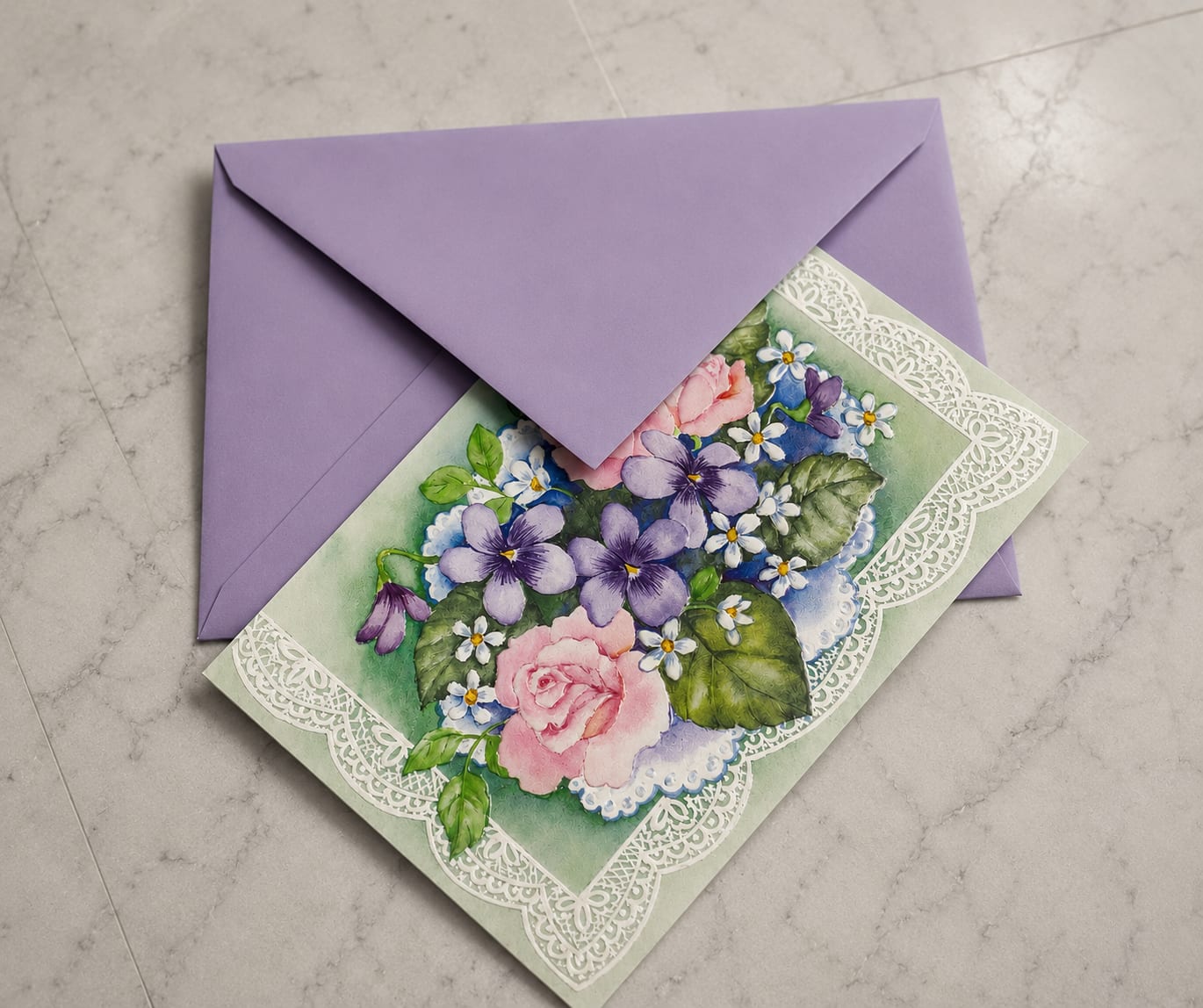 Personalized Handwritten Cards - A soft lavender envelope and a handwritten greeting card that reads like a warm springtime note-this greeting set is perfect as an add-on for birthdays, thank-you bouquets, or a simple thinking-of-you surprise. The card pairs a vintage-inspired watercolor floral cluster-pink roses, purple pansy-like blooms, little white filler flowers and fresh green accents-with ornate lace-paper trim to give the recipient a handmade, sentimental moment alongside their flowers.  The card and envelope arrive ready to tuck into any flower arrangement or to send on their own; the front artwork mirrors the purple, pink, white, and green palette of many bouquets, so it complements roses and mixed arrangements beautifully. The delicate lace edging and soft watercolor texture create a tactile, keepsake quality that makes the message feel more personal; include your handwritten note and we'll enclose it in the lavender envelope for delivery.  Ideal for spring celebrations, anniversaries, or just because, this greeting card turns a floral gift into a memorable moment the recipient will cherish. Select personalization at checkout and we'll handwrite your message and seal it in the envelope so it's ready to present with your flowers.