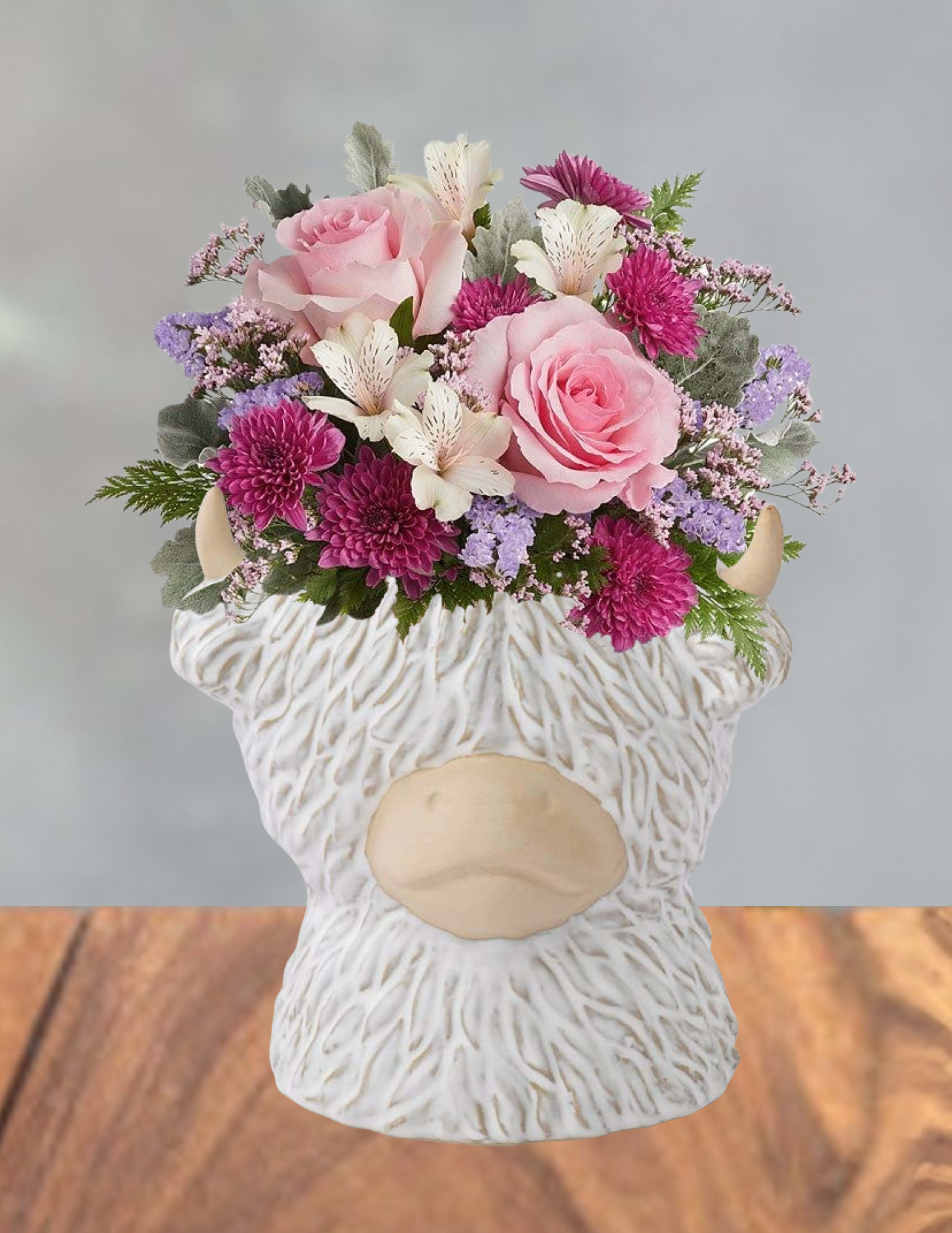 Moos and meadows  - Soft pink roses and bright magenta chrysanthemums give this flower arrangement a cheerful, feminine glow-perfect as a birthday bouquet or a playful anniversary surprise. The design reads like a stroll through spring meadows, with white alstroemeria and small lavender filler blooms framing the roses to create a compact, rounded silhouette that catches the eye and feels delightfully intimate for the person you're celebrating.  The blooms are arranged with silvery-green foliage for texture and contrast, delivering a layered mix of pink, white, purple, and green that plays well in both modern and cottage-style rooms. Everything sits in a white ceramic bull-shaped vase with a textured surface and beige horns, a whimsical hard-good that doubles as a keepsake decorative piece once the flowers fade. Sized to be a cheerful tabletop accent, this arrangement arrives ready to display and makes a thoughtful, memorable gift that says you picked something distinctive just for them.