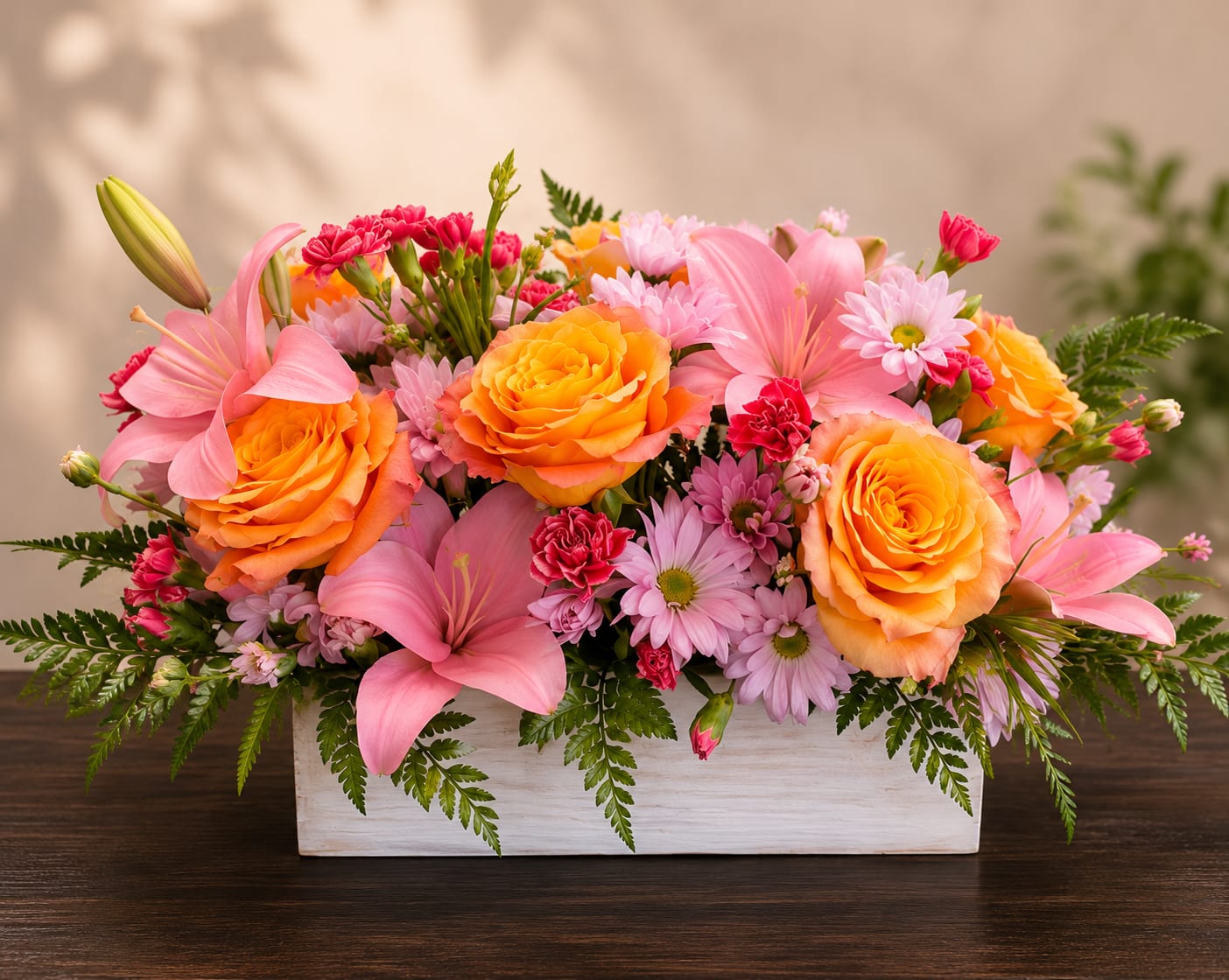 Armonía de Primavera - A lively, garden-style flower arrangement that greets the recipient with exuberant spring color - perfect as a birthday bouquet, a cheerful get-well gift, or a just-because surprise. This low, dense flower arrangement places the arrangement type and occasion front and center so the person you're thinking of feels brightened and celebrated the moment they see it.  Pink lilies open at the center surrounded by warm orange roses, lavender daisy-like blooms, and small red carnations, all set in a clean white rectangular vase. Pale pink tones soften the palette while fern-like foliage spills around the edges for a full, abundant silhouette; the compact, low profile makes it ideal for a tabletop, desk, or dining centerpiece without blocking conversation.  Send this arrangement to mark spring occasions or everyday moments when you want someone to feel noticed and joyful. The white rectangular container provides easy placement and a modern contrast to the vivid blooms - order sizing and delivery options at checkout; care is simple: fresh water and a cool spot will keep the flowers looking their best.