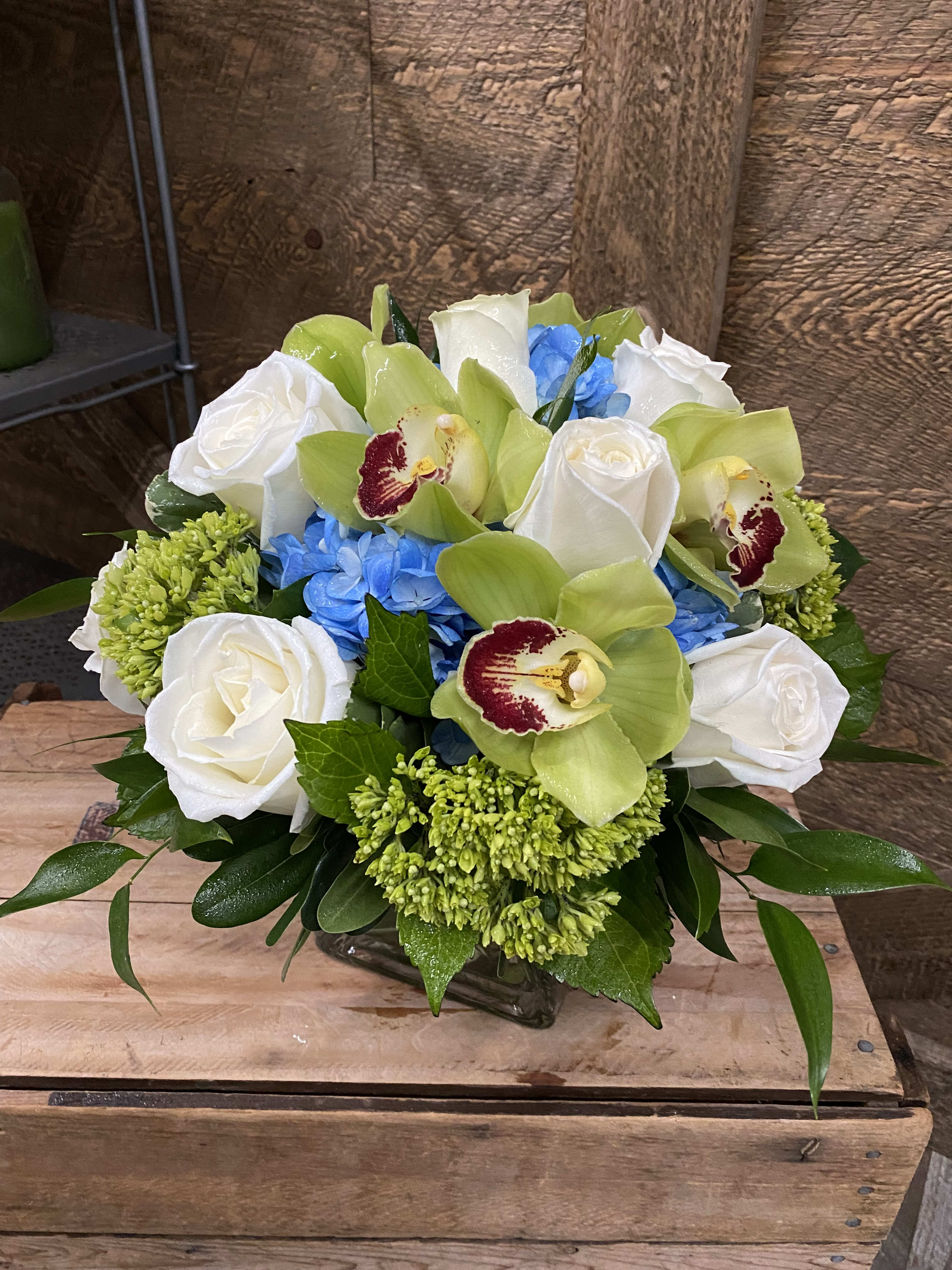 Bouquet of white roses, green orchids, and blue hydrangeas in a glass vase