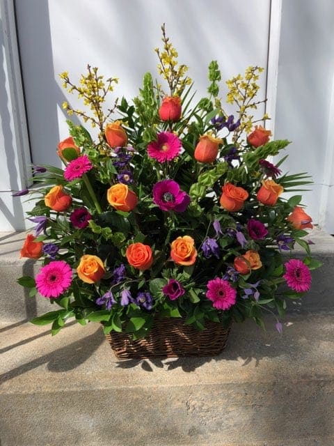 Basket arrangement of orange roses, pink gerberas, and purple flowers