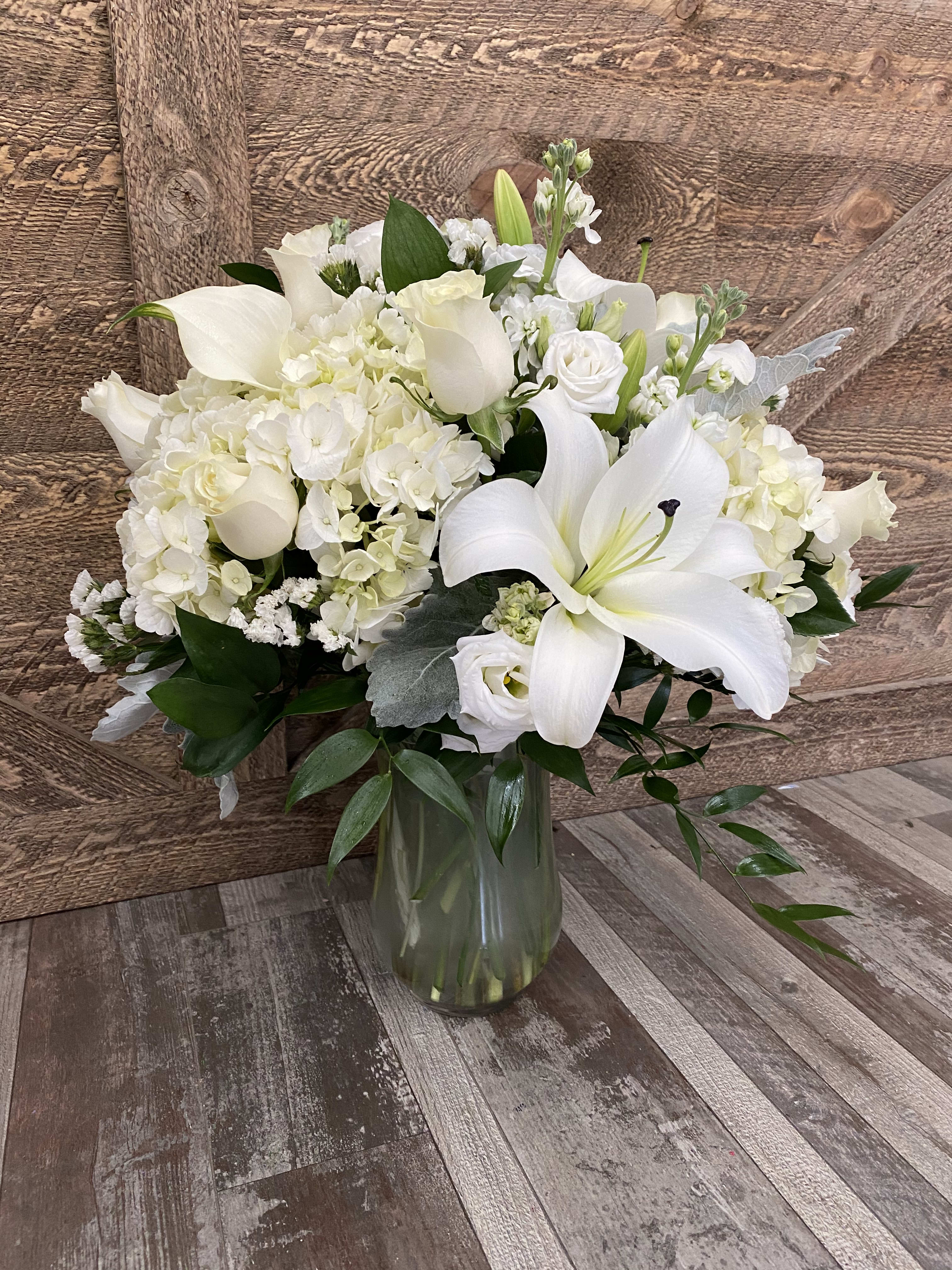 White floral arrangement with lilies, hydrangeas, and calla lilies in a glass vase