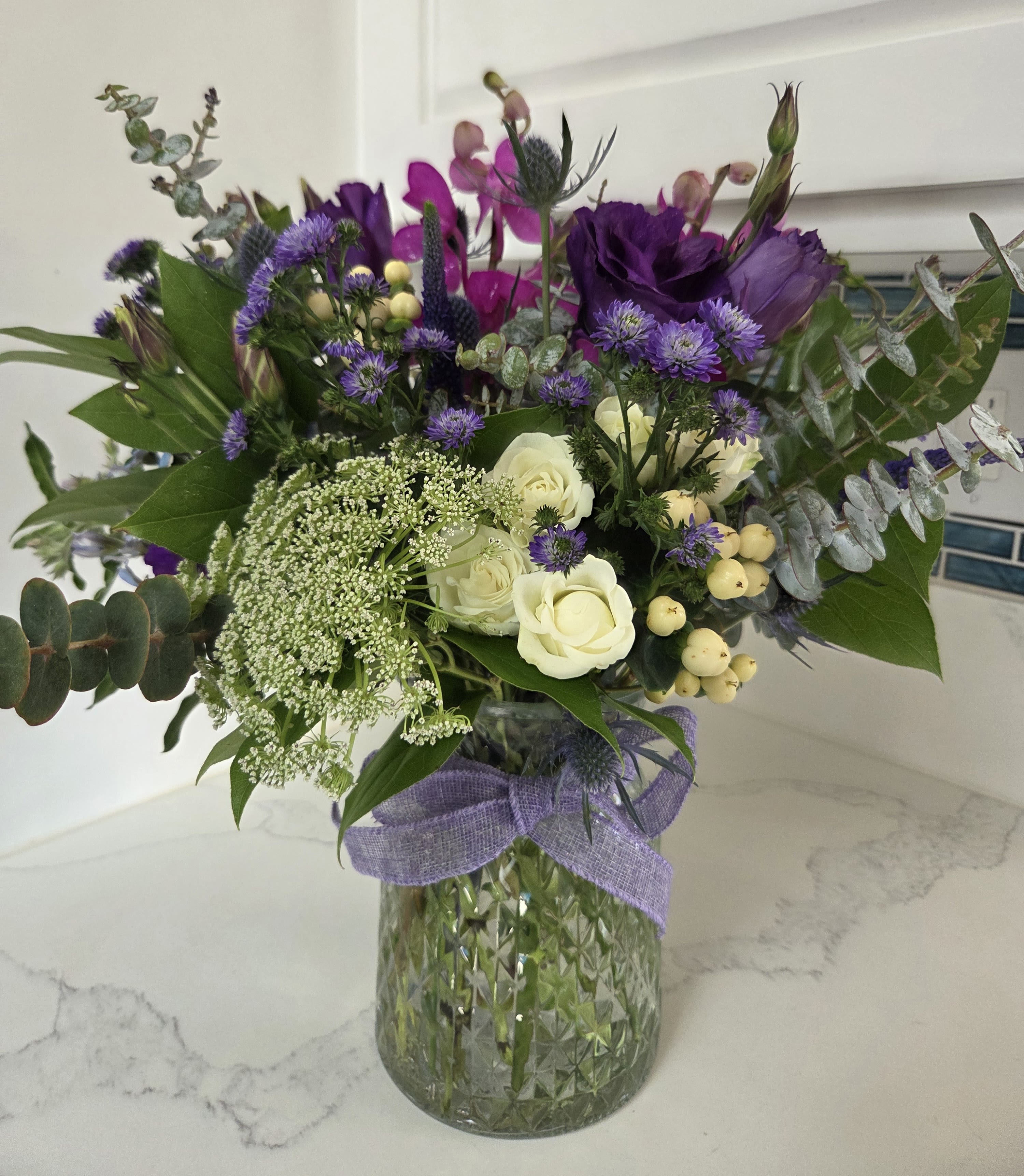 Moody Blue - This floral arrangement features rich, moody shades of blue, purple and green, artfully blended to create a lush and sophisticated display that is sure to delight. Displayed in a clear glass vase.
