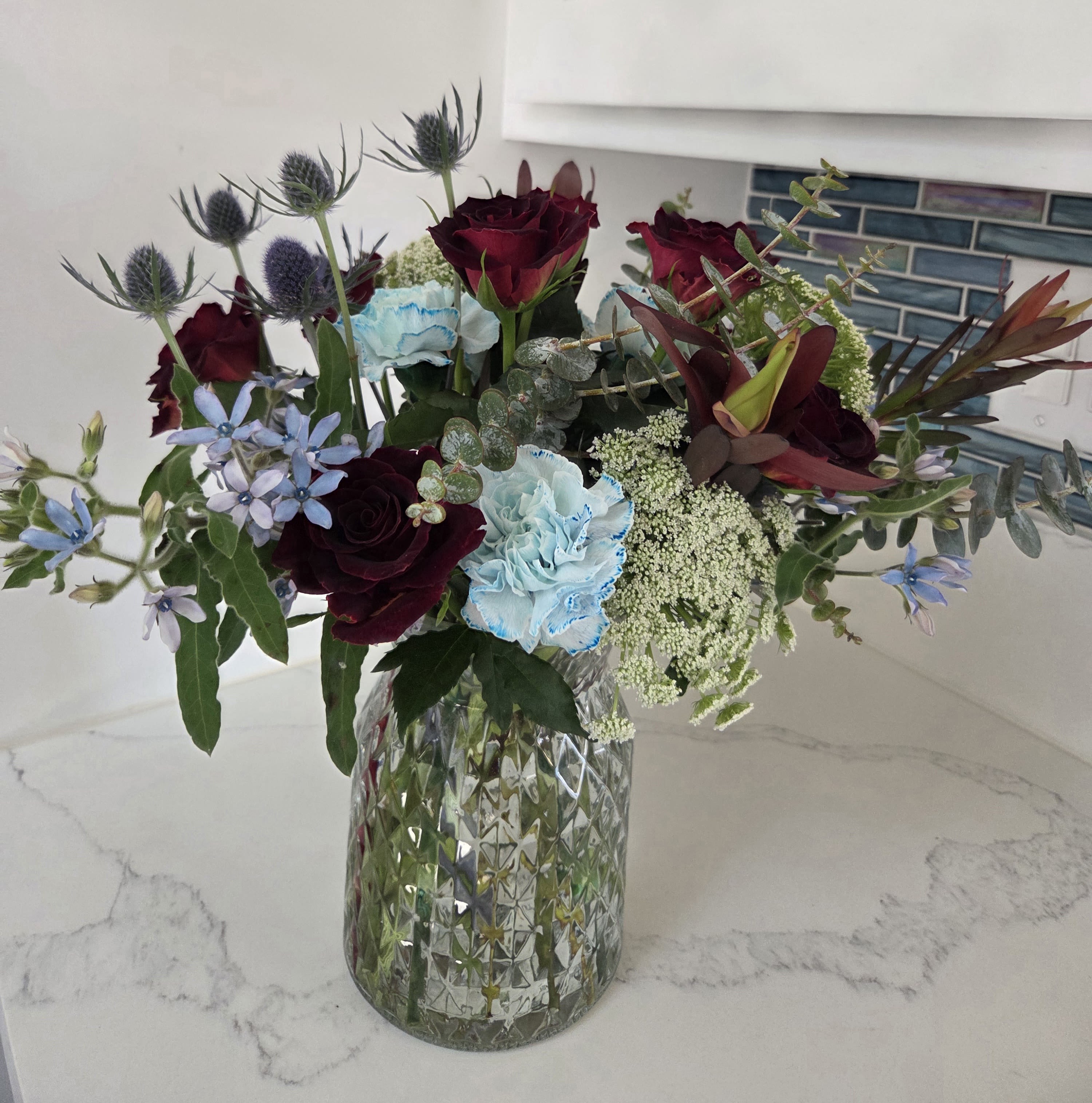 Red, White and Bloom - A unique collection of red, white and blue stems thoughtfully gathered to create a patriotic display full of color and texture. Displayed in a clear glass vase.