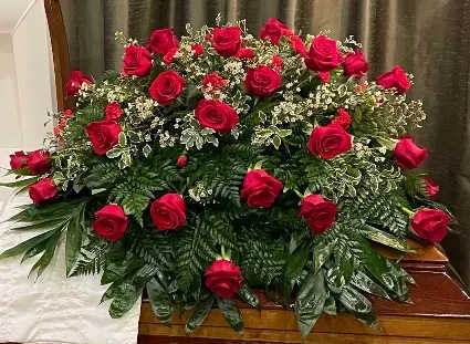 Treasured Memories - A dense mound of velvety red roses set against clusters of delicate white filler and rich dark green foliage-this sympathy flower arrangement offers a quietly powerful way to honor a life. As a funeral or memorial tribute, the red-and-white palette reads as both respectful and heartfelt, the rounded, full design conveying care and presence for the person you're remembering.  The arrangement is crafted in a lush, layered style with blooms arranged across the top and sides to create a substantial, garden‑like dome. Deep red roses form the visual anchor while tiny white accents brighten the composition and the green leaves provide a structured, calming backdrop. Its scale and formal color contrast make it equally appropriate for an intimate service, a graveside tribute, or to send to family at home.  Made to comfort and to convey sincere regard, this piece is designed to make the recipient feel honored and seen during a difficult moment. Order with confidence for a funeral, memorial, or to send condolences-our team prepares each arrangement fresh so the flowers arrive ready to express your sympathy.