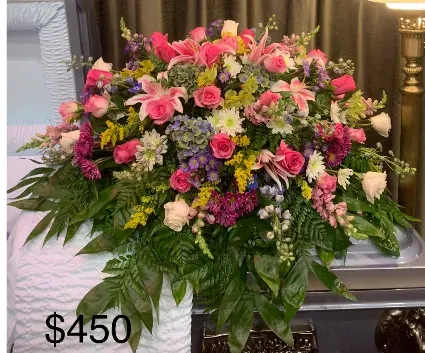 Vibrant Life - A large, full casket spray that brings a comforting, uplifting presence to a funeral or sympathy service, Vibrant Life pairs classic roses and lilies with soft hydrangea to create a heartfelt tribute. The pink and white blooms read as gentle and respectful while touches of purple and yellow add subtle warmth-perfect for honoring a life with both tenderness and color.  This arrangement is dense and layered over abundant greenery, forming a broad, cascading composition that softly drapes the casket. Roses, lilies, hydrangeas and carnations are mixed with smaller filler blooms in purple and yellow, and long foliage extends outward to soften the edges and create a substantial, formal silhouette suited to traditional memorial settings.  Designed to comfort the people you're thinking of, Vibrant Life sends a message of sympathy and celebration of the person's spirit-she'll feel genuinely honored and remembered. For sizing and delivery details, please select the casket-spray option at checkout or contact us for custom color adjustments or local delivery arrangements.