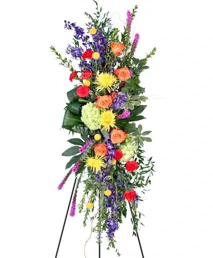 Consoling Colors Standing Spray - Consoling Colors stands as a vibrant testament to love and remembrance. With the rich hues of red carnations, purple liatris, orange roses, and yellow spider mums and billy buttons, each bloom weaves a tapestry of warmth and consolation, offering solace in its radiant display. Order this standing spray to offer you heartfelt sympathy.  Includes: With, Aspidistra, Baby Blue Eucalyptus, Coccullus, Fatsia, Myrtle, Variegated Pittosporum, Italian Ruscus, Red Carnations, Green Hydrangeas, Yellow Billy Buttons, Deep Blue Delphinium, Purple Liatris, Orange Roses, Yellow Spider Mums.