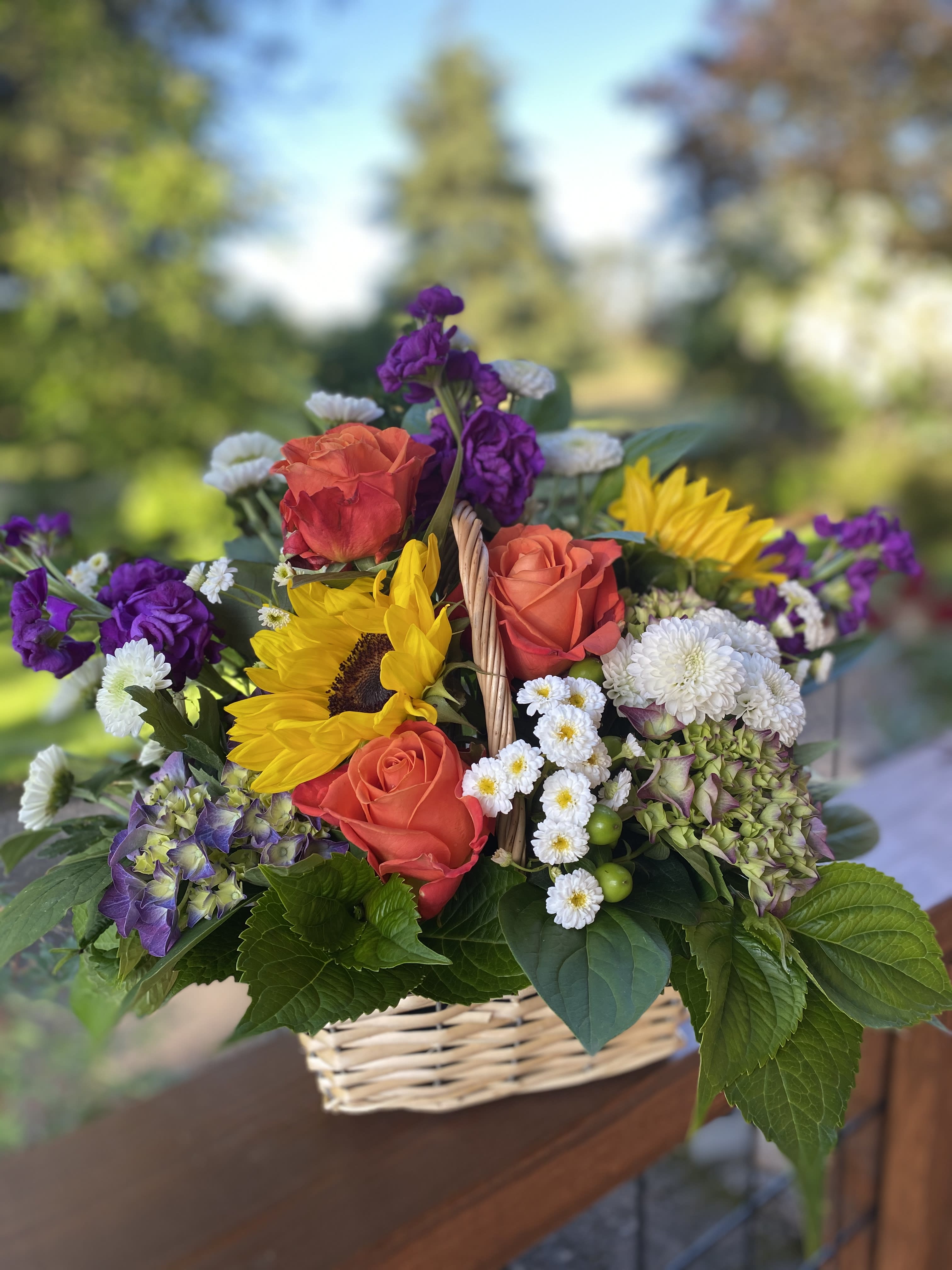 Basket arrangement with orange roses, sunflowers, and purple blooms